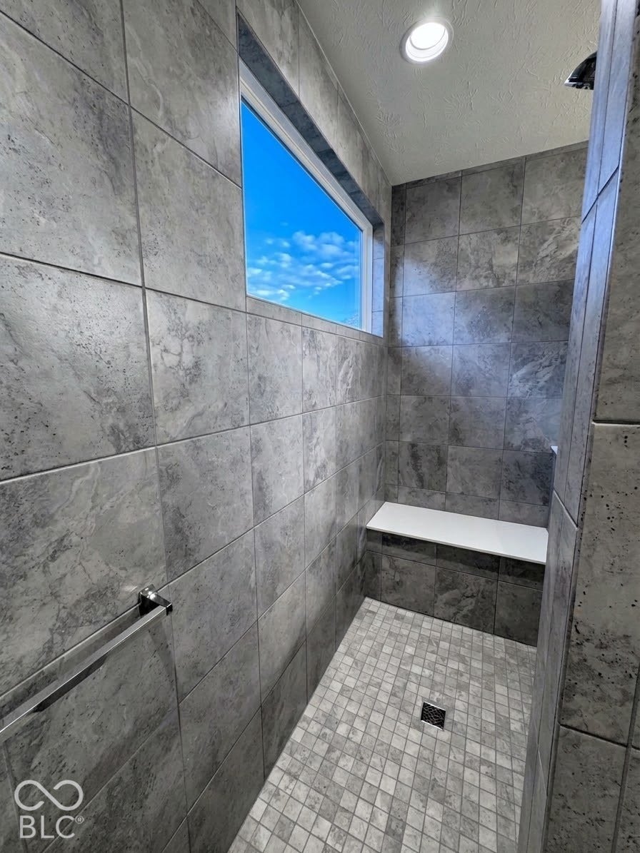 Tiled shower with a built-in bench, mosaic floor, horizontal window, and recessed lighting