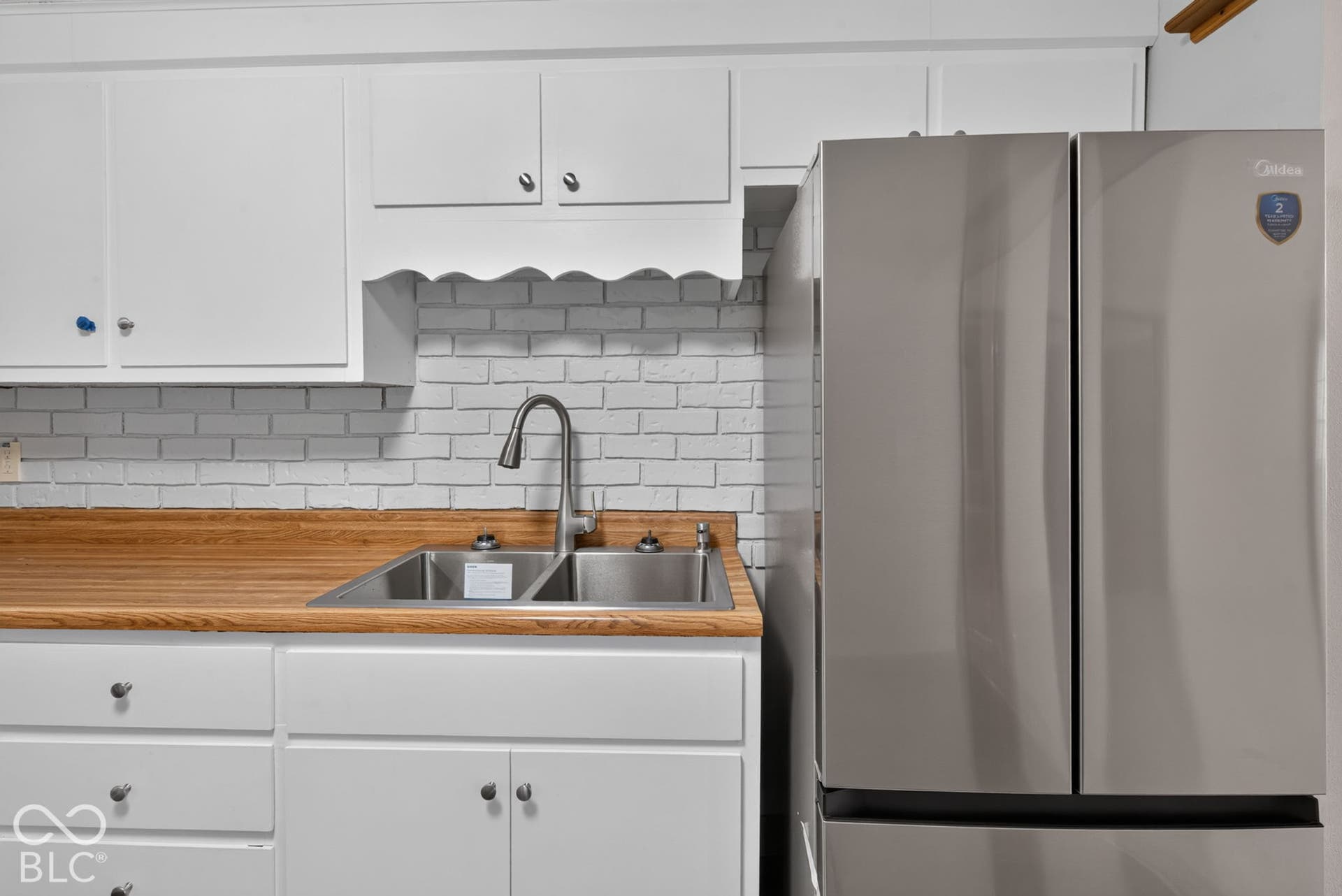 White cabinetry, wood-finish countertops, subway tile-style backsplash, stainless steel double-basin sink, and a stainless steel French door refrigerator