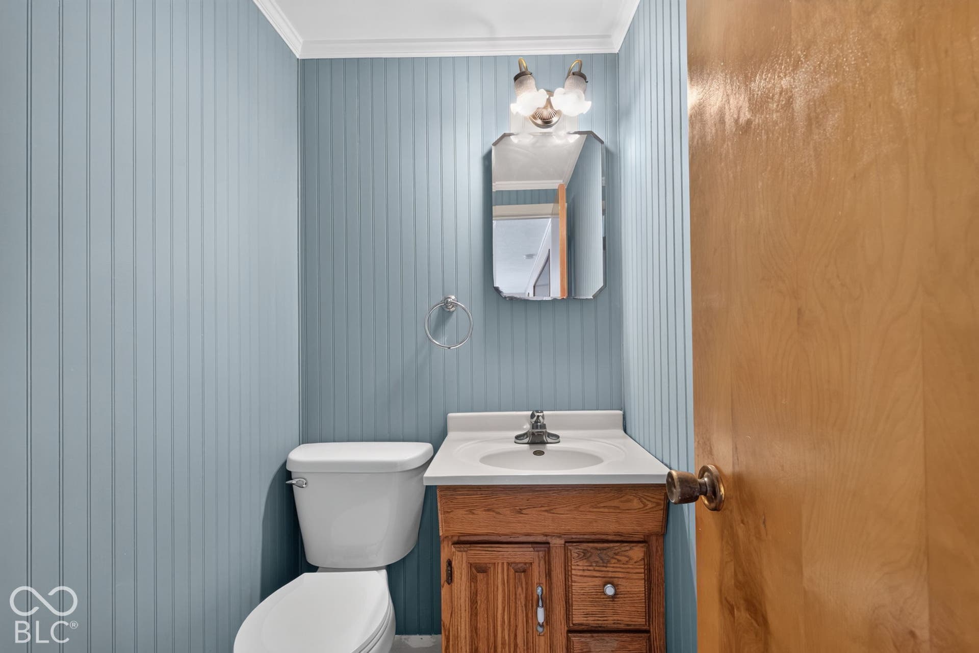 Powder room featuring vertical wall paneling, a wooden vanity with a built-in sink, a wall-mounted mirror, and a two-bulb vanity light fixture