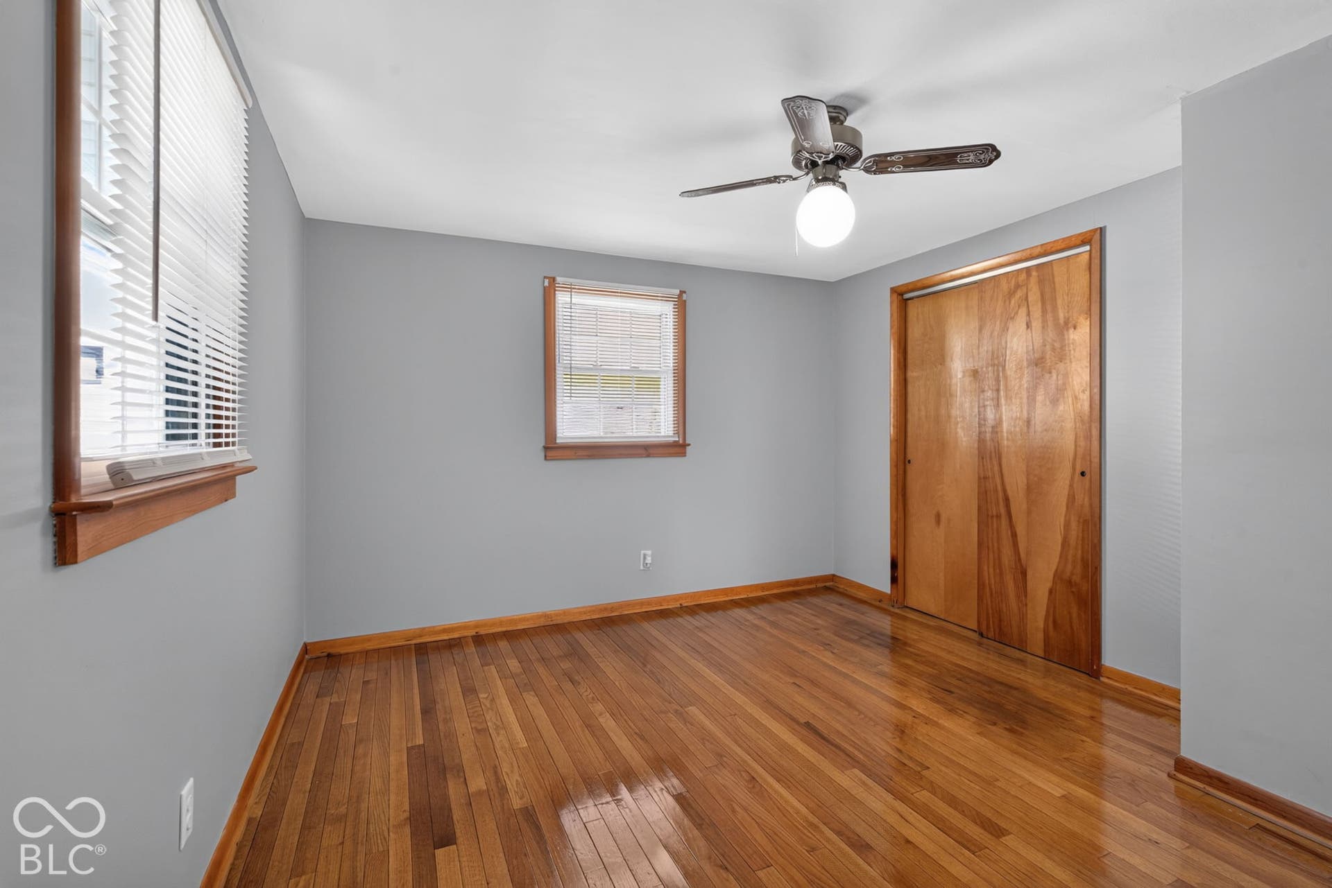Hardwood flooring with coordinating wood trim, two windows, and a ceiling fan with integrated lighting