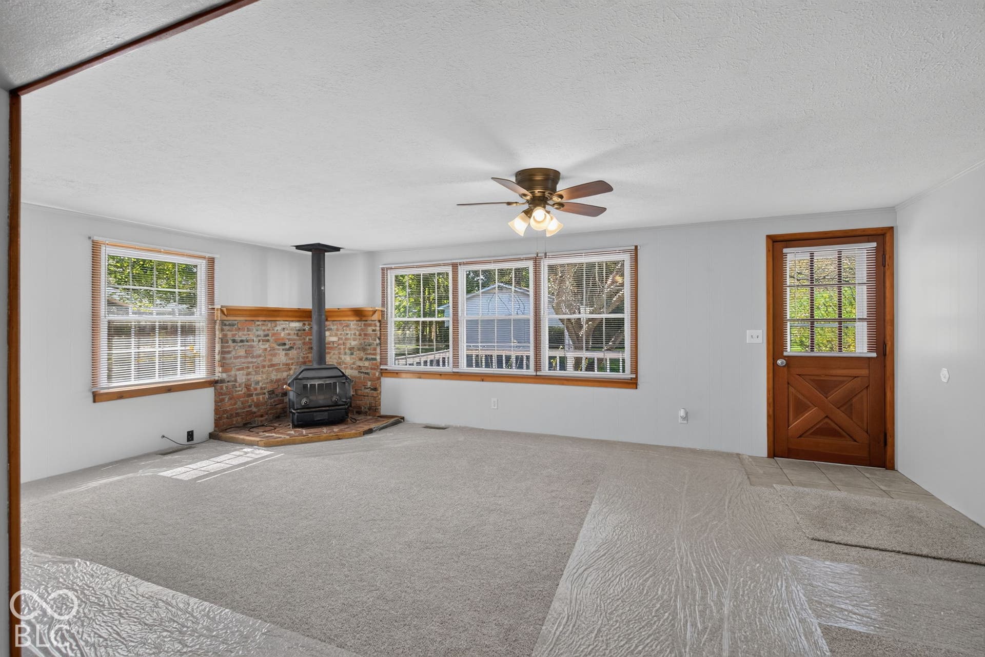 Living area featuring a brick hearth with a freestanding wood stove, multiple windows, a wood-finish door, and a ceiling fan