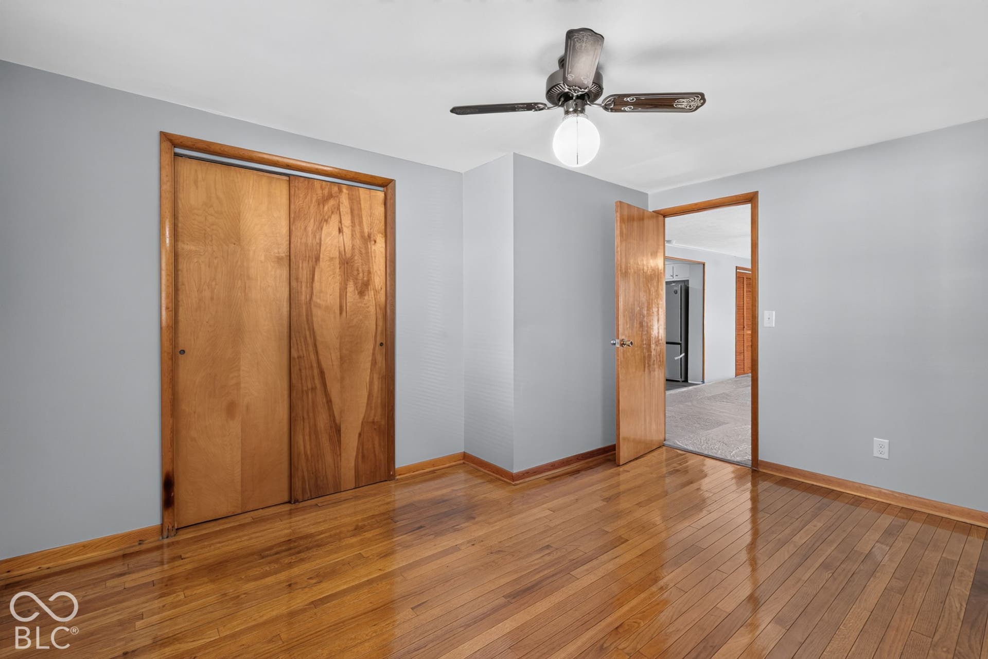 Hardwood flooring, light gray wall paint, wood-finish doors, and a ceiling fan with integrated lighting