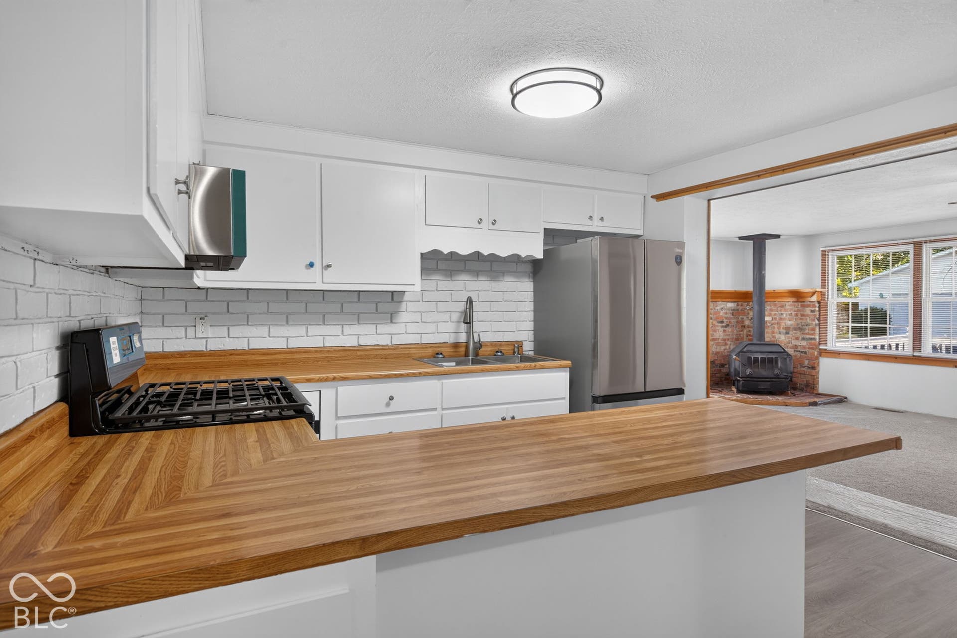 Wood-finish countertops, subway tile backsplash, stainless steel refrigerator, white cabinetry, and a gas range