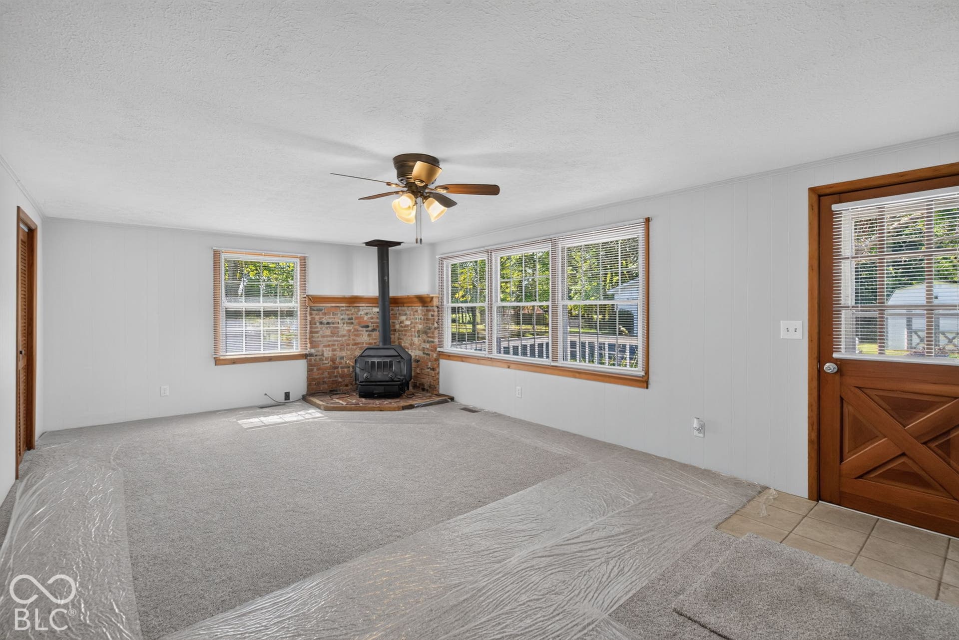 Living area featuring a brick accent wall, a freestanding stove, multiple windows, a ceiling fan, and a wood-finish entry door