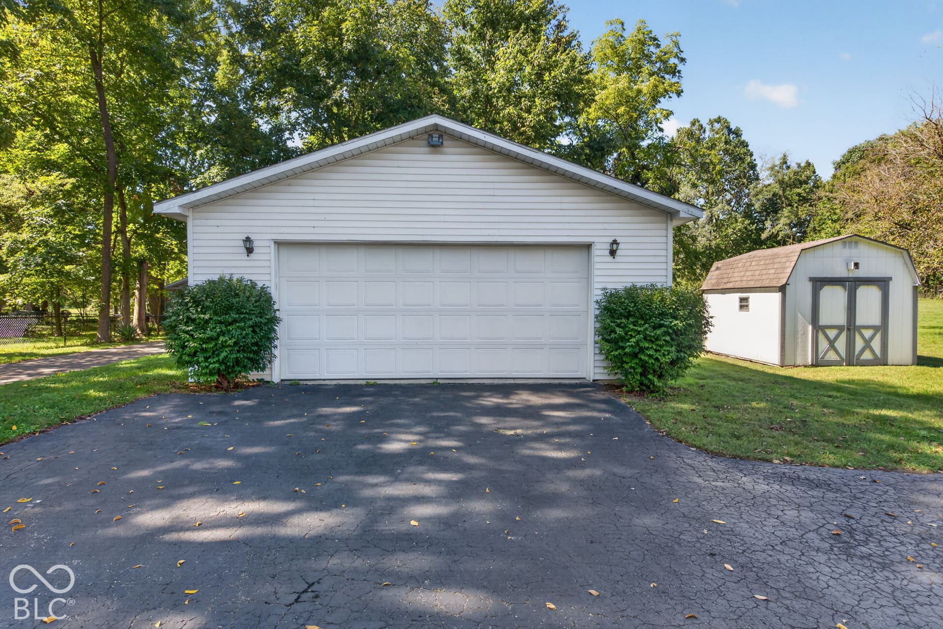 Two-car garage with white paneled door, exterior wall lanterns, and gabled roof