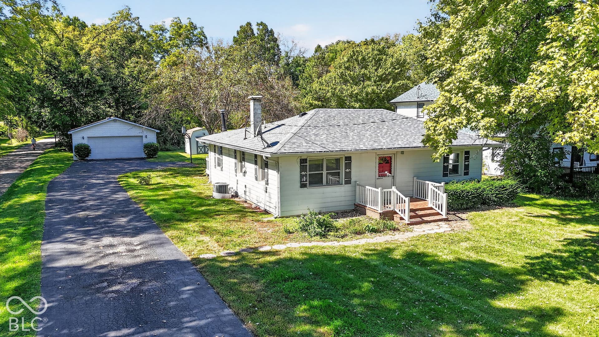Single-story residence with a pitched shingle roof, paved driveway, detached two-car garage, and mature landscaping