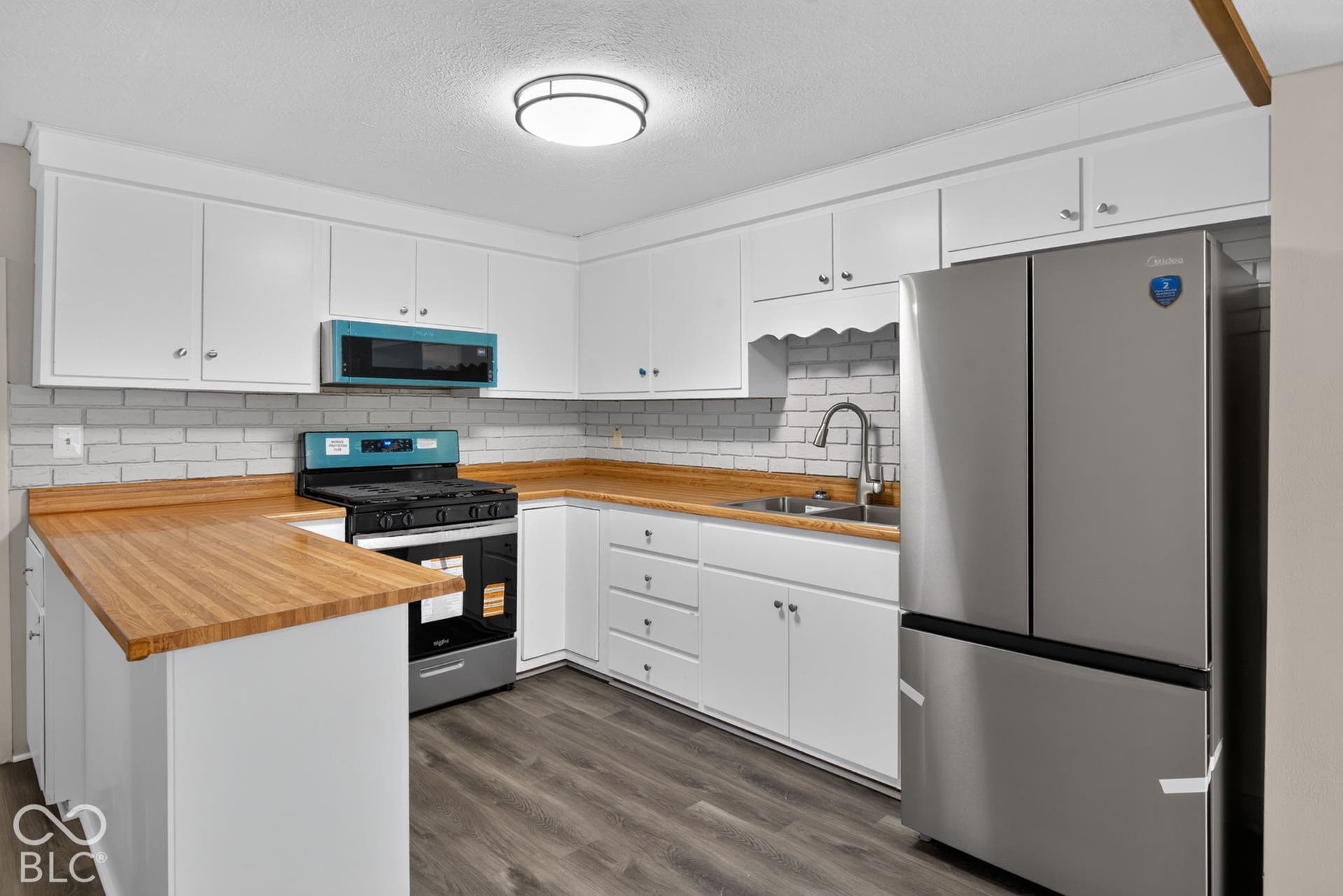 White cabinetry with brushed nickel hardware, wood-finish countertops, stainless steel appliances, subway tile backsplash, and wood-look flooring