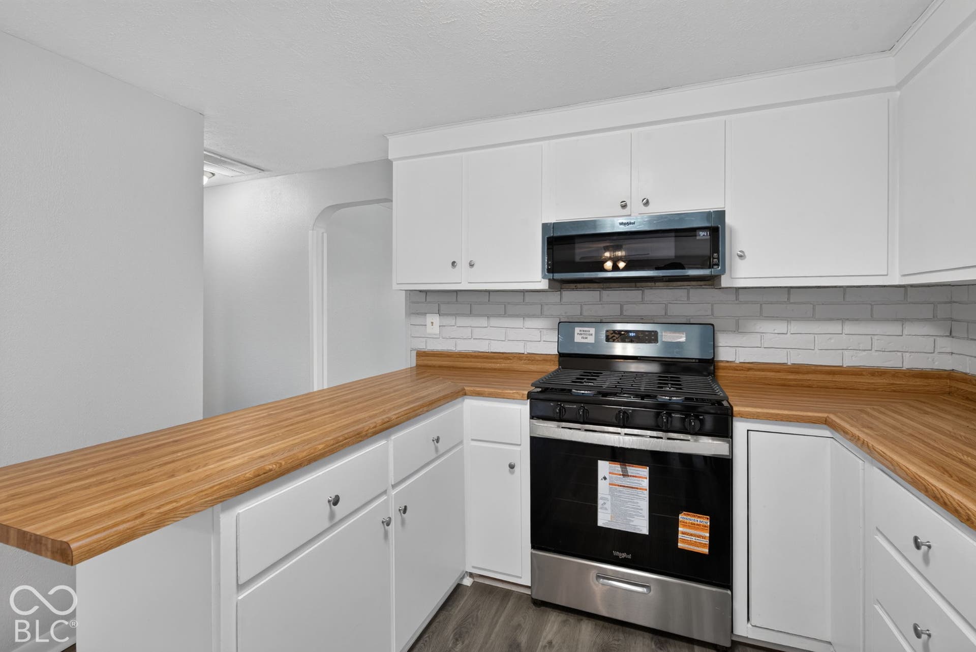 White cabinetry with silver hardware, wood-finish countertops, subway tile backsplash, stainless steel gas range, and a built-in microwave