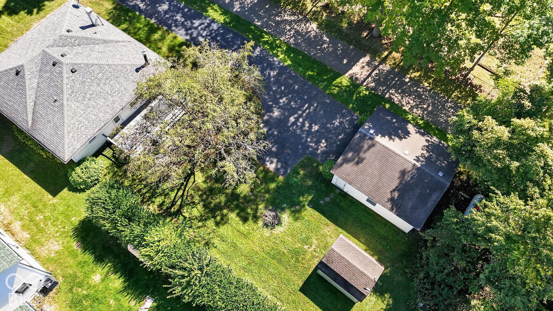 Property featuring a main residence with a multi-pitched roof, a detached structure with an asphalt roof, a secondary detached structure with an asphalt roof, and an asphalt driveway
