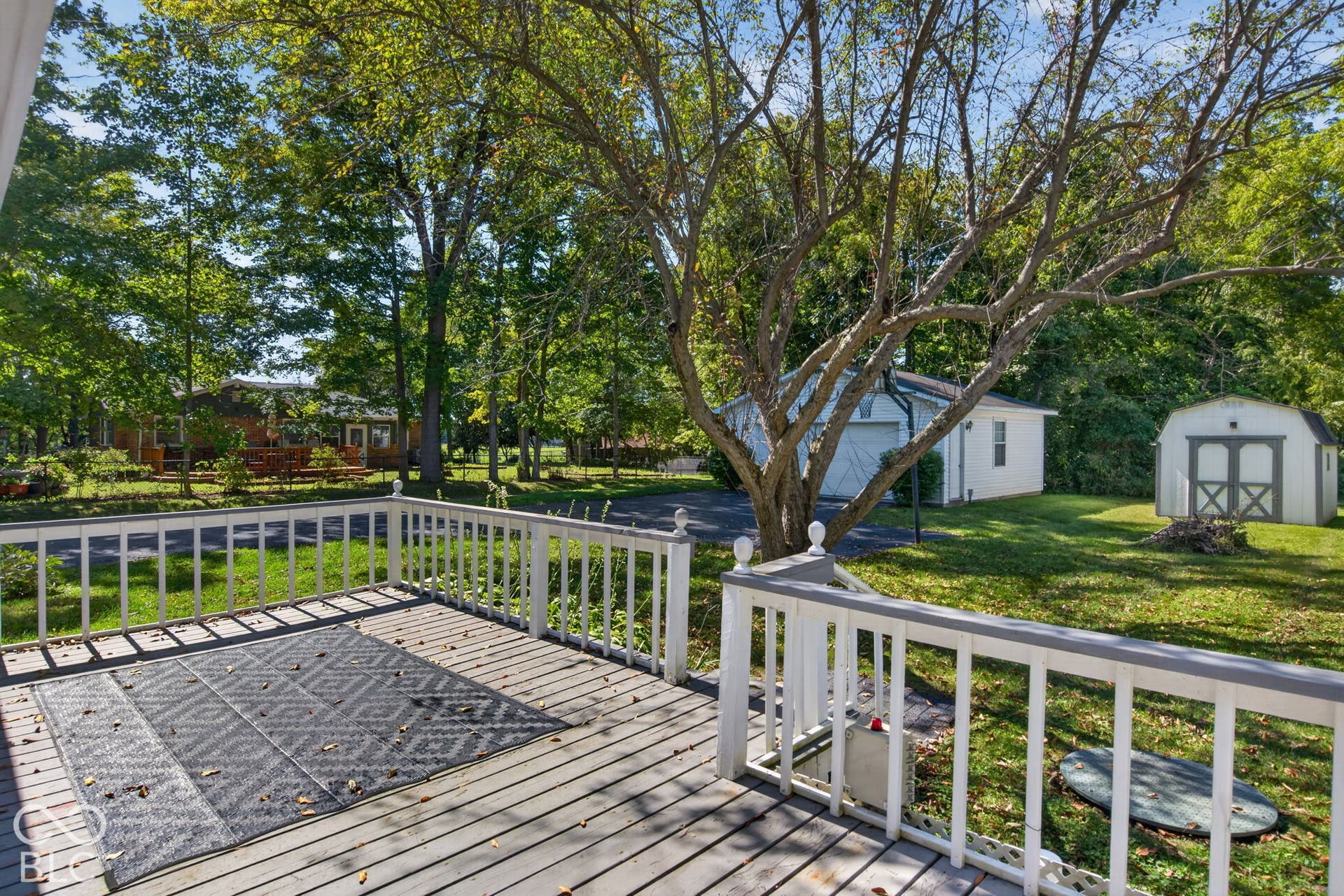 Expansive wood deck with white railings, offering a broad yard area with a detached garage and a storage shed