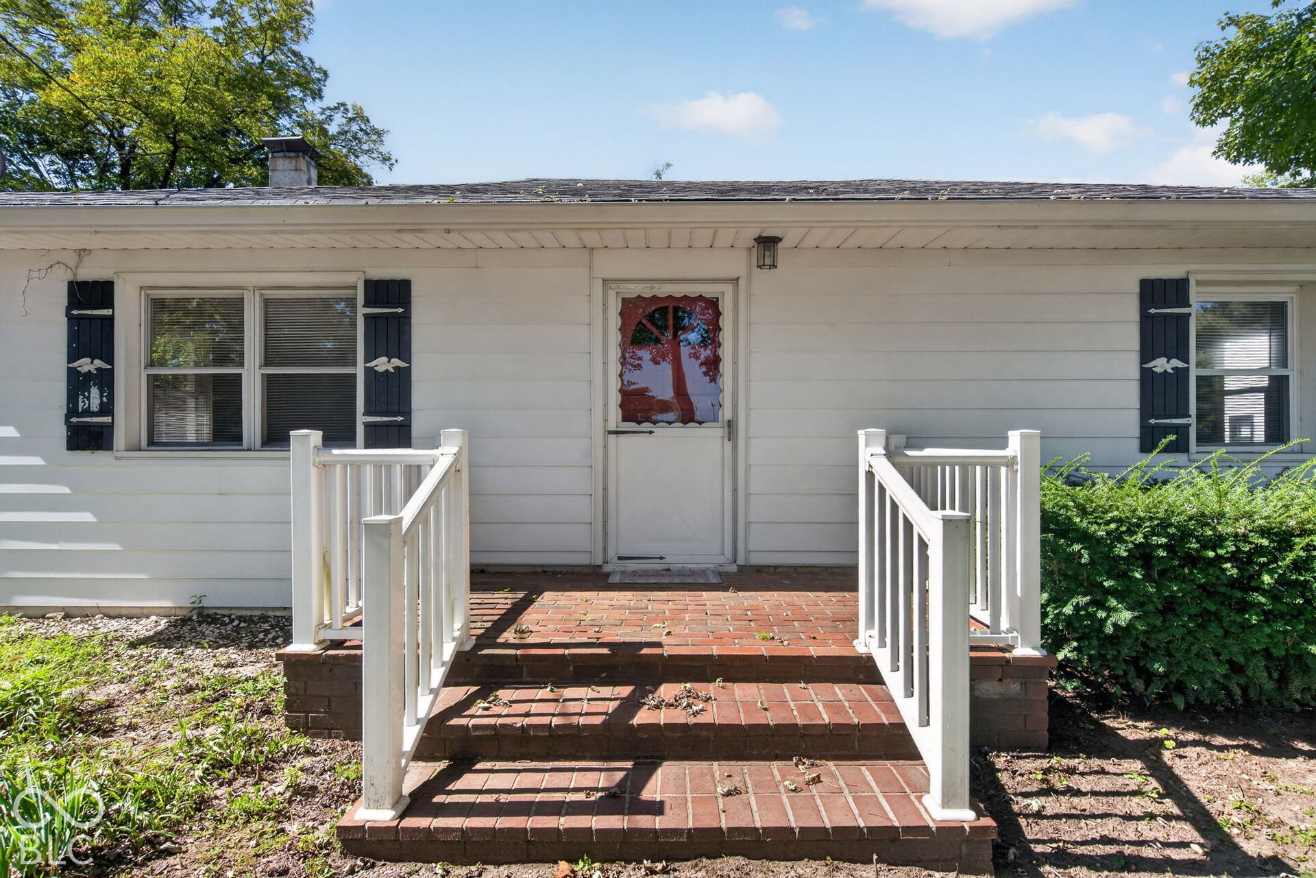 Brick steps with white railings, white siding exterior, and dark shutters