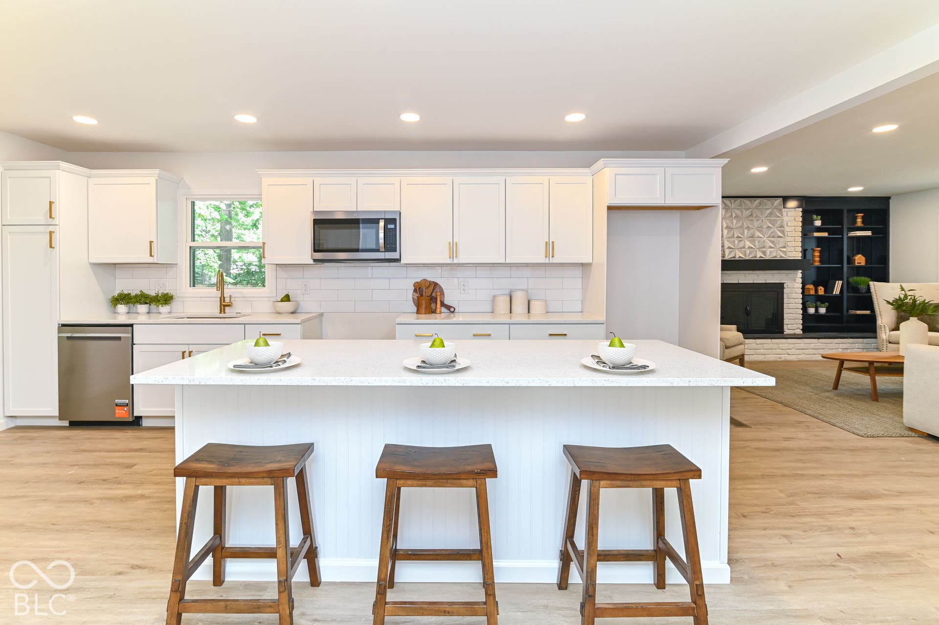 White shaker cabinetry, stainless steel appliances, central island with seating, wood-finish flooring, and subway tile backsplash