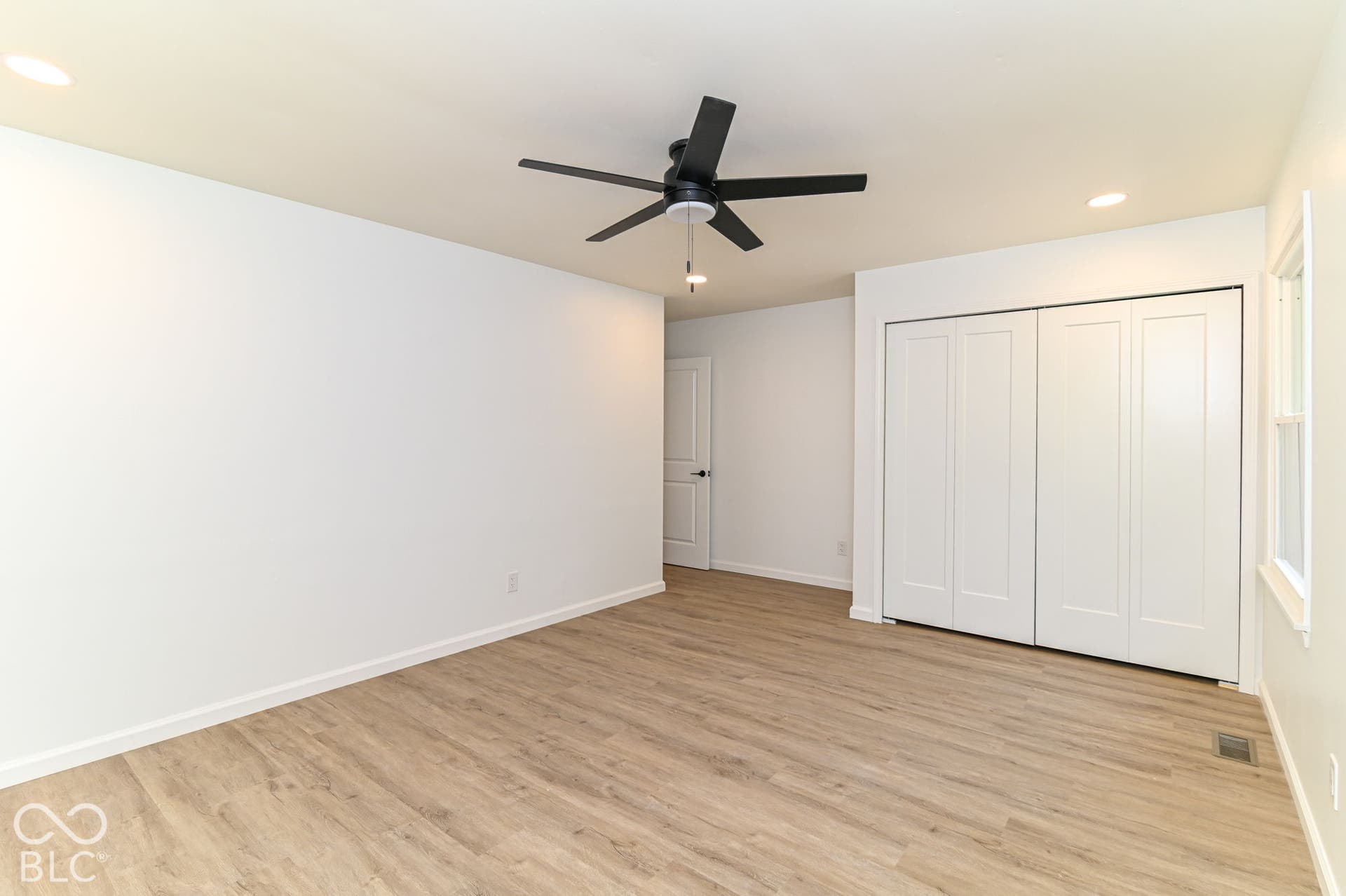Wood-finish flooring, recessed lighting, ceiling fan, white paneled bifold closet doors, and white walls