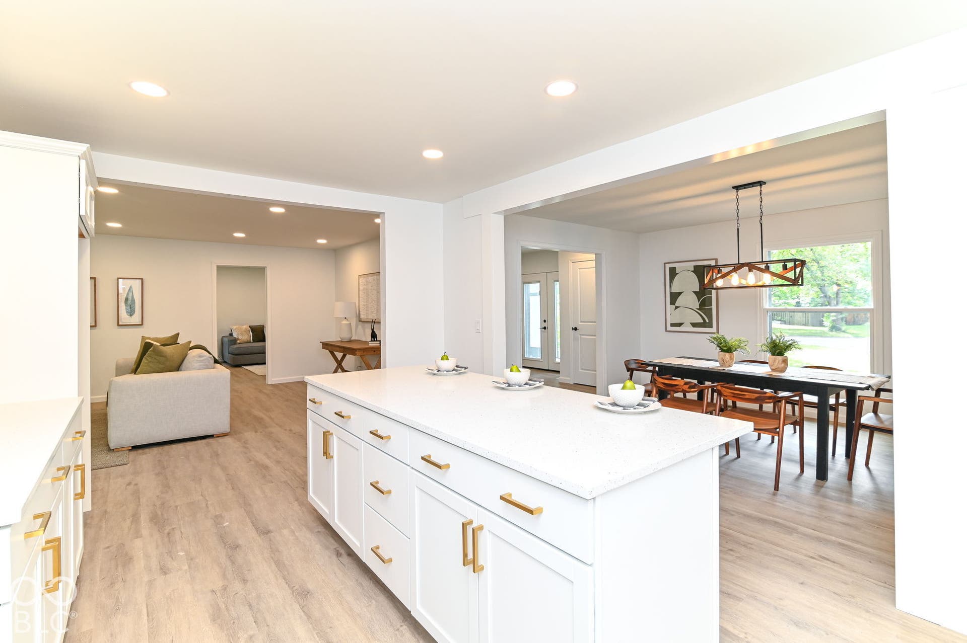 Kitchen island with a light-toned countertop and gold-toned hardware, wood-finish flooring, recessed lighting, and a dining area with a rectangular chandelier
