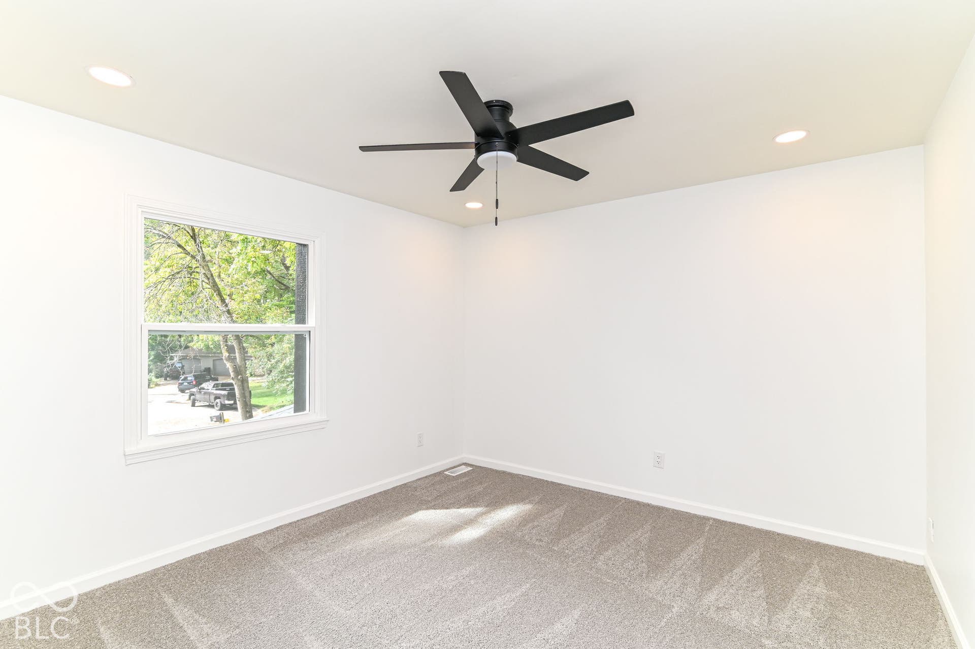 Recessed lighting, ceiling fan, white walls, carpet flooring, and a double-hung window