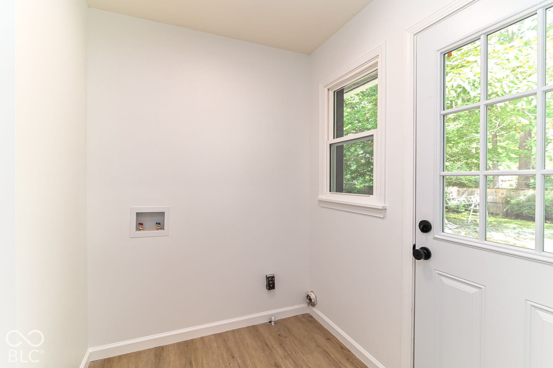 White paneled door with black hardware, double-hung window, and wood-finish flooring