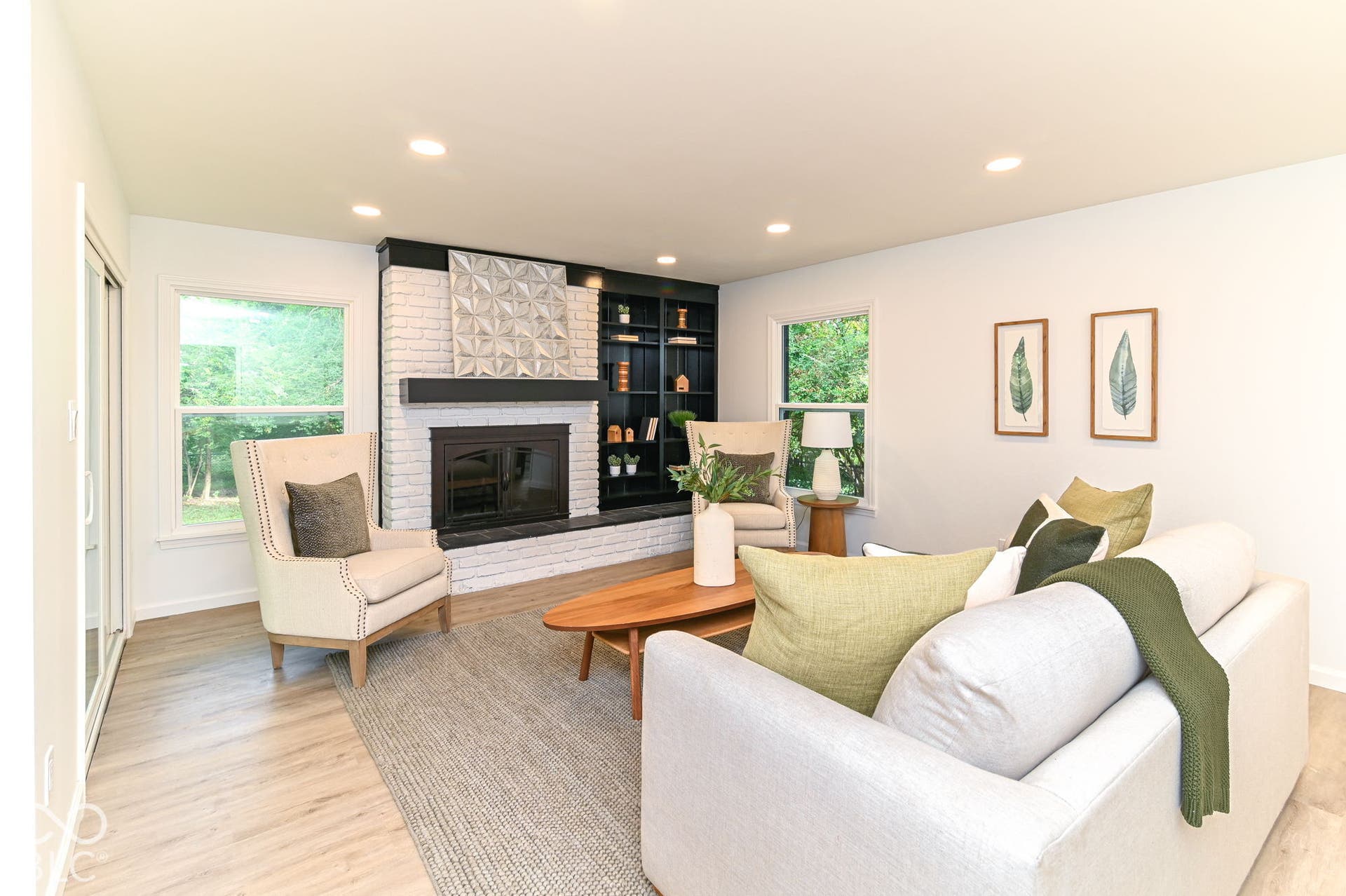 Recessed lighting illuminates the living area, featuring wood-finish flooring and a white brick fireplace with a dark mantel