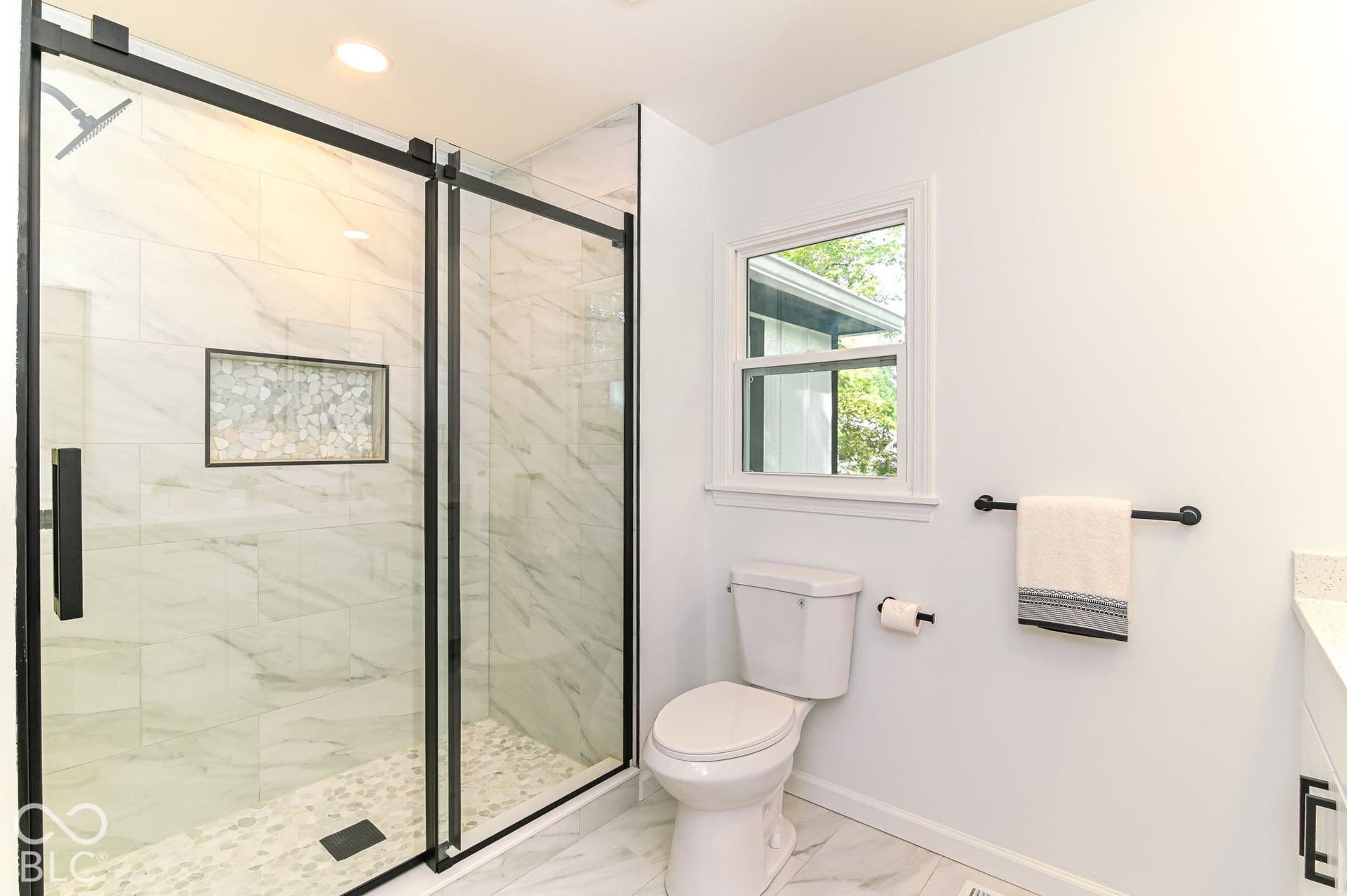 Enclosed shower with black-framed glass doors, a rainfall showerhead, and a tiled niche
