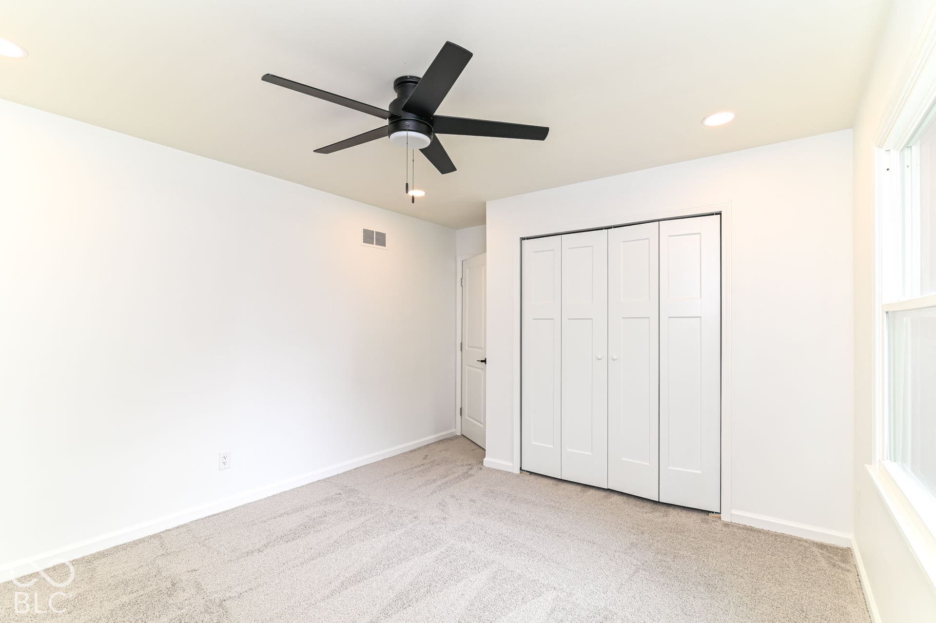 White walls, gray carpet, matte black ceiling fan, recessed lighting, and white bi-fold closet doors
