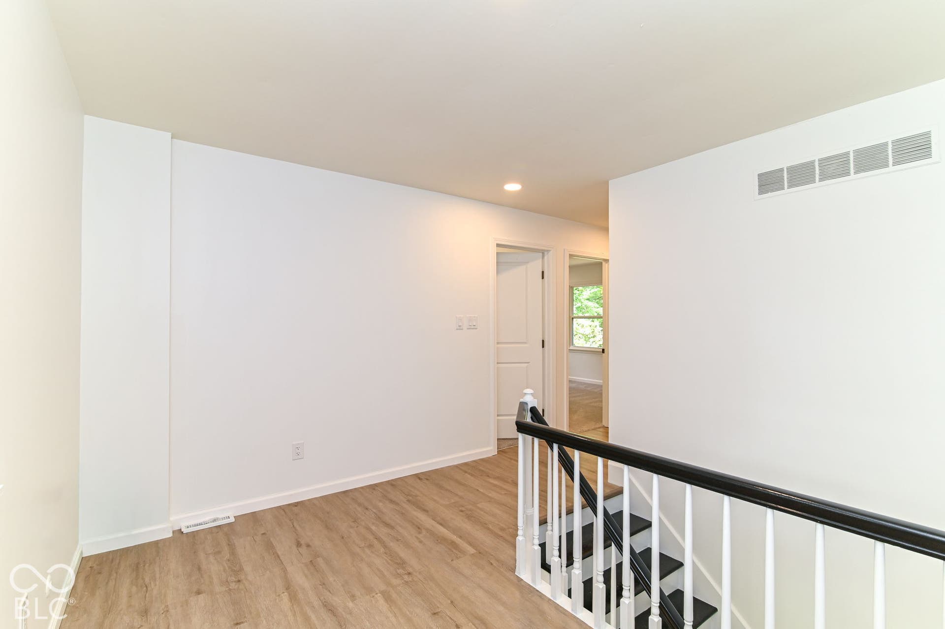 Wood-finish flooring, white walls, and a black and white staircase railing