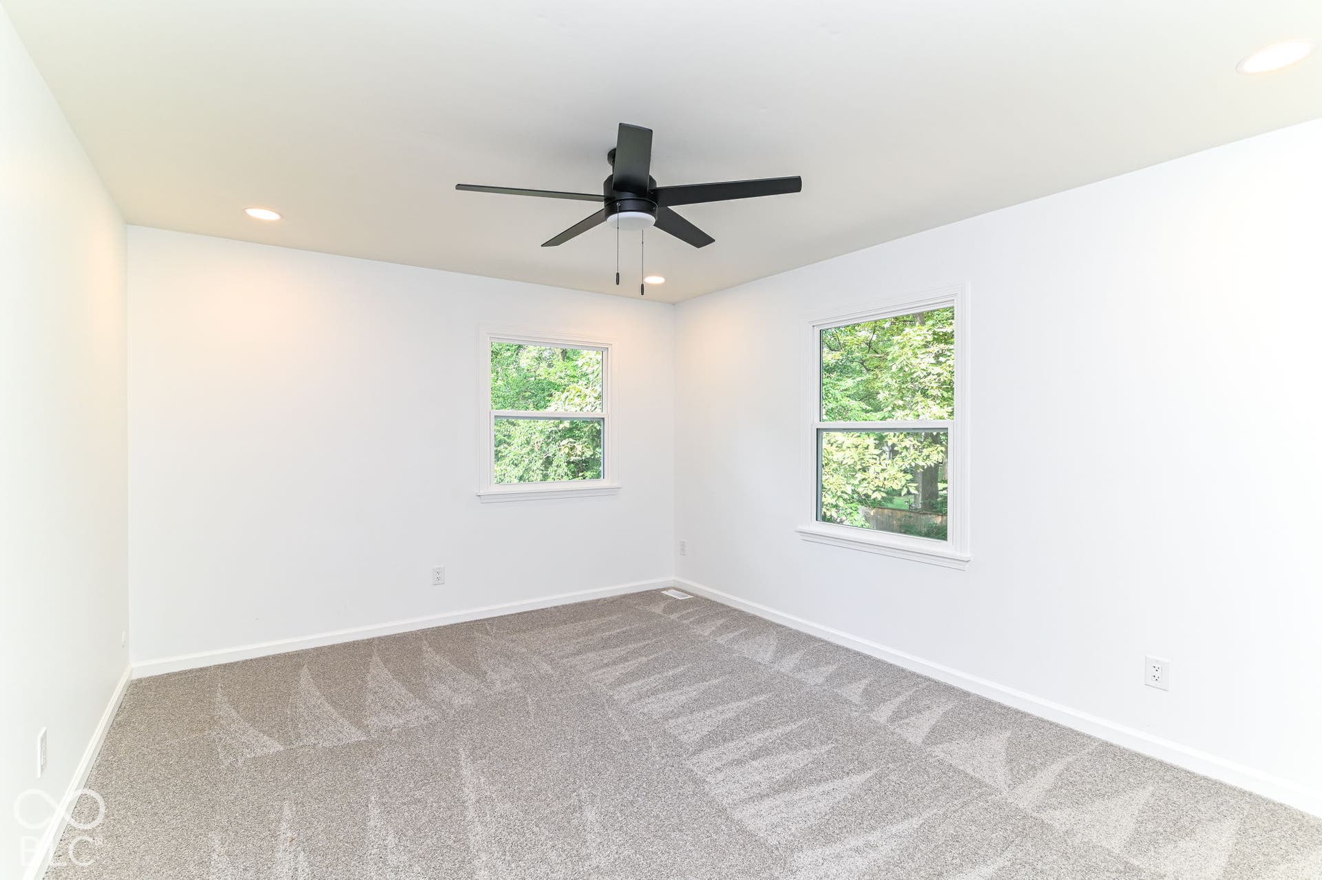 Neutral gray patterned carpet, dual windows, recessed ceiling lighting, and a black ceiling fan