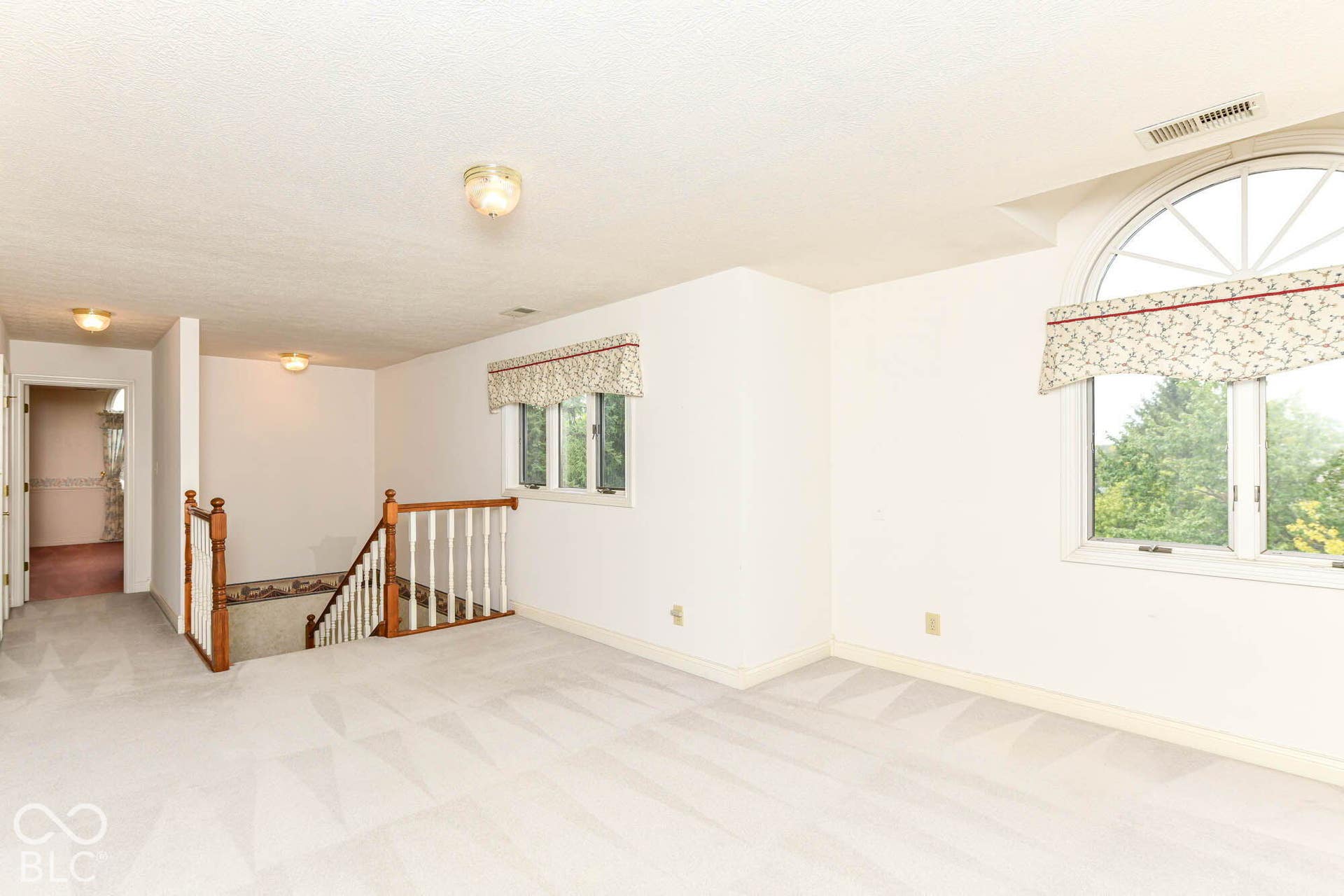 6431 Shamel Drive, Indianapolis, IN 46278 Loft. Expansive carpeted area featuring a large arched window, multiple flush-mount light fixtures, and a staircase with wood handrails