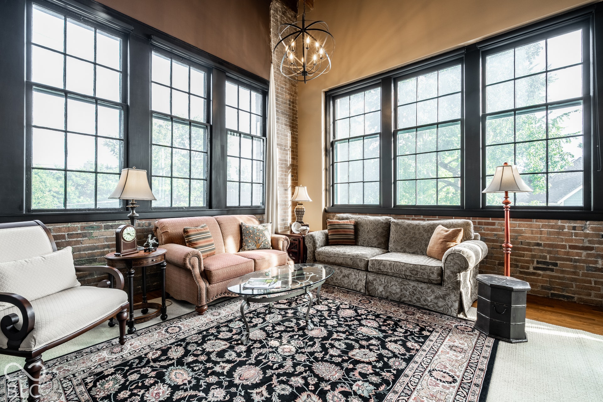 High ceilings, exposed brick wall, hardwood flooring, large grid windows, and an industrial-style chandelier