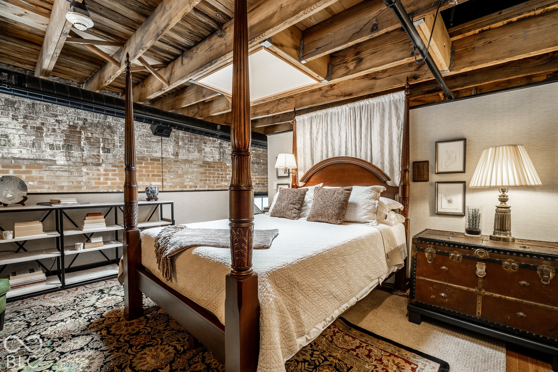 Exposed wood beam ceiling, exposed brick wall, built-in shelving, and a prominent four-poster bed frame