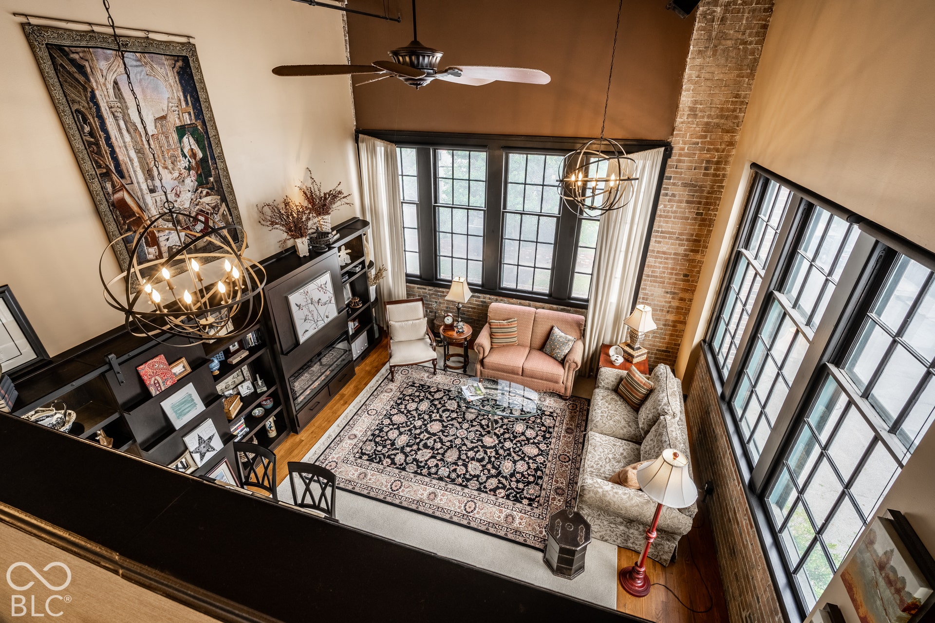 Two-story living area with exposed brick accents, dark-framed multi-pane windows, wood-finish flooring, and a built-in media console with shelving