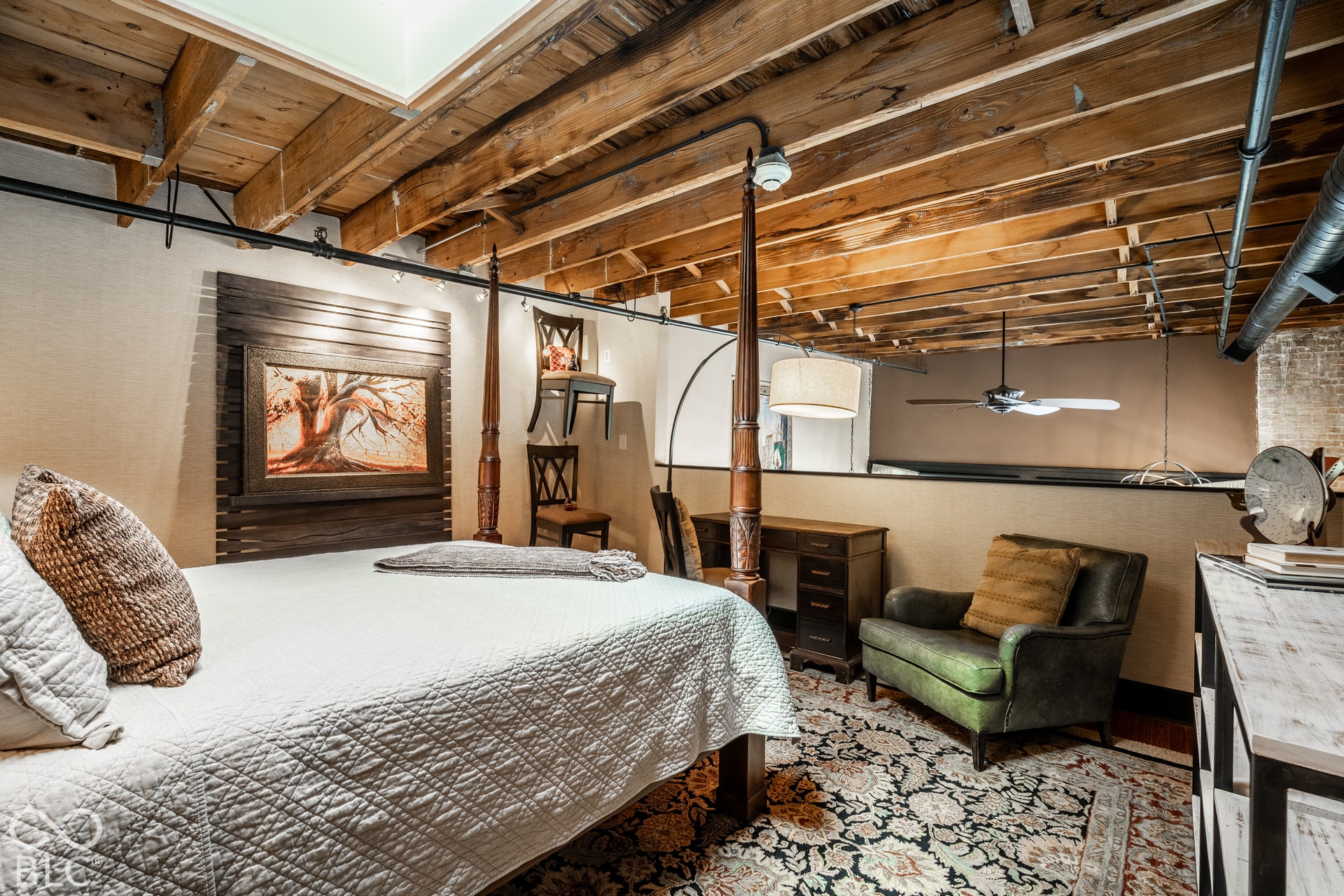 Exposed wood beam ceiling, wood-finish flooring, wood-paneled wall accent, track lighting, and a ceiling fan
