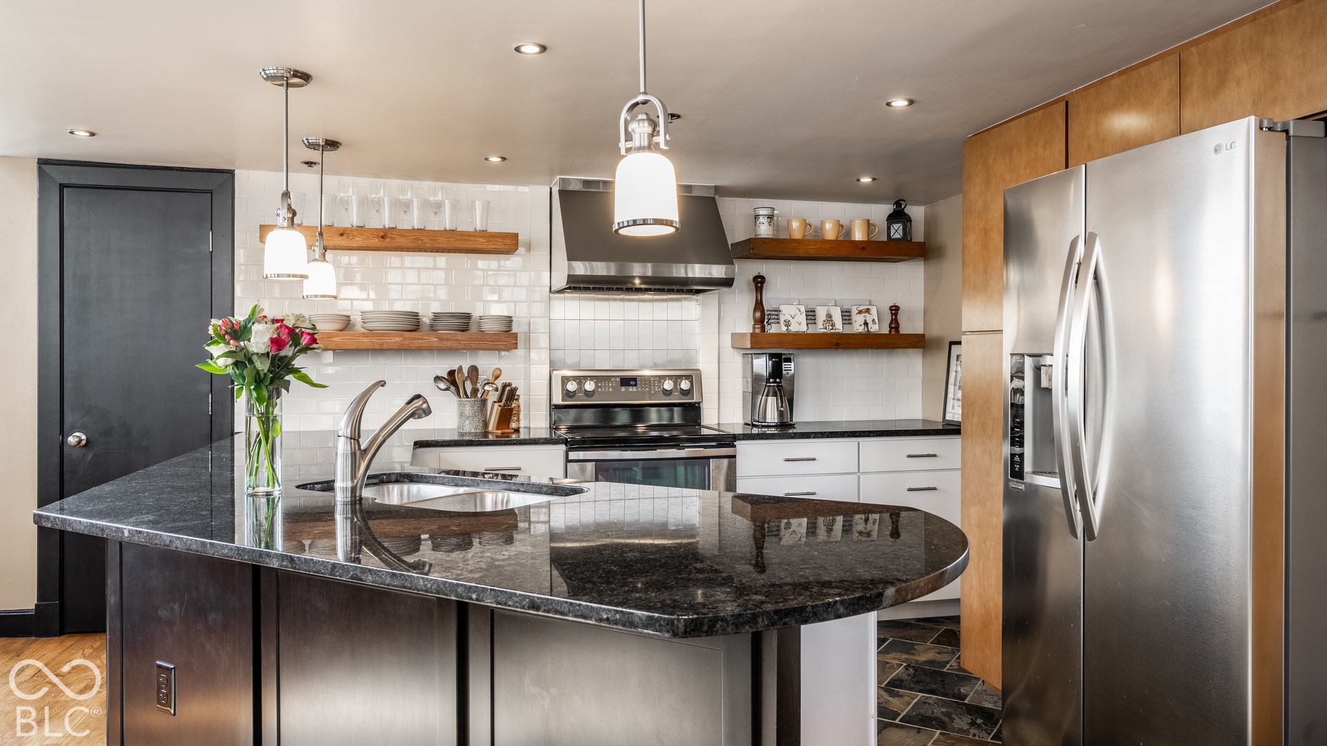 Kitchen featuring an expansive island with a built-in sink, stainless steel appliances, open wood shelving, recessed lighting, and pendant lighting fixtures