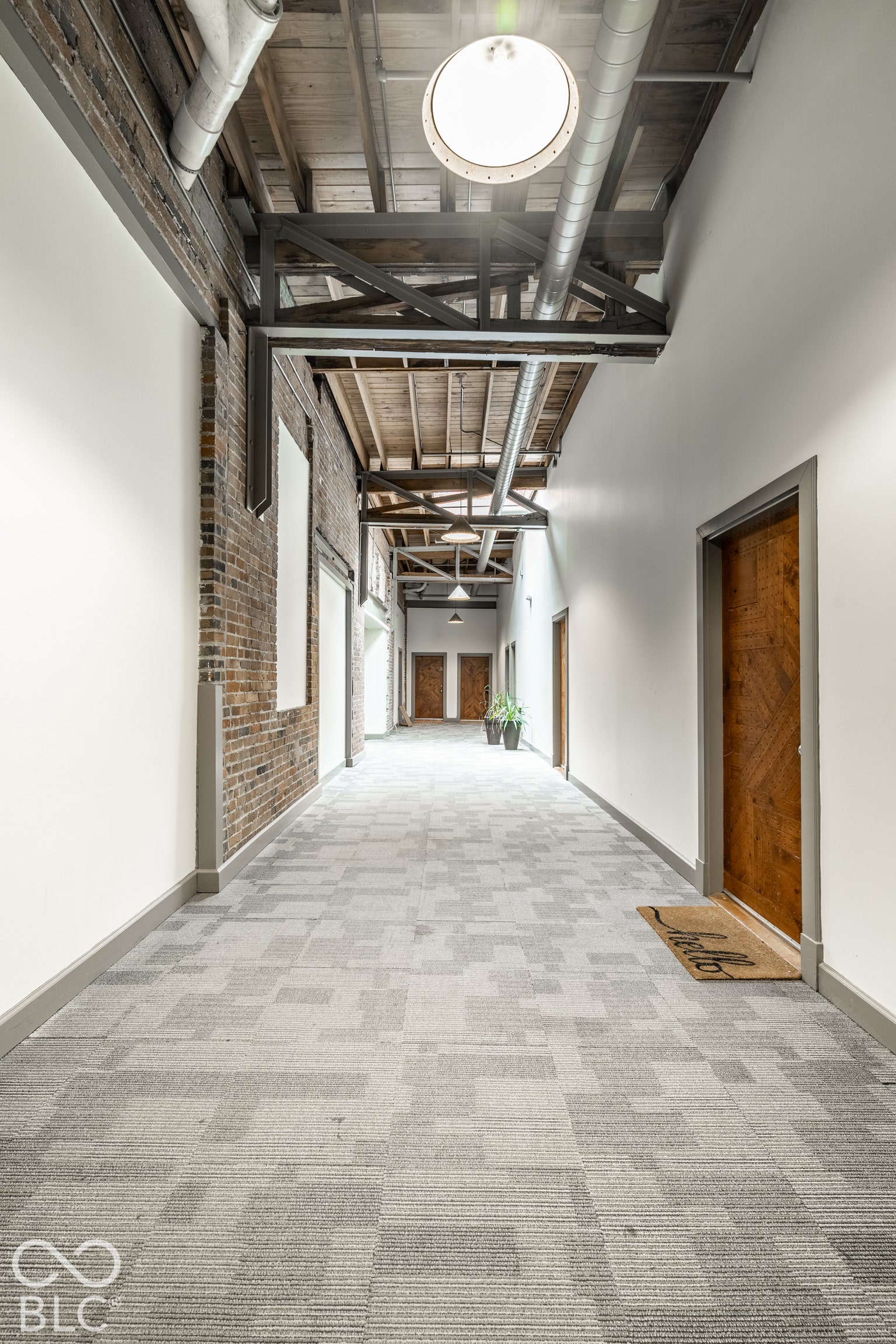 Exposed brick wall, open wood beam ceiling, exposed ductwork, recessed lighting, and patterned carpet flooring