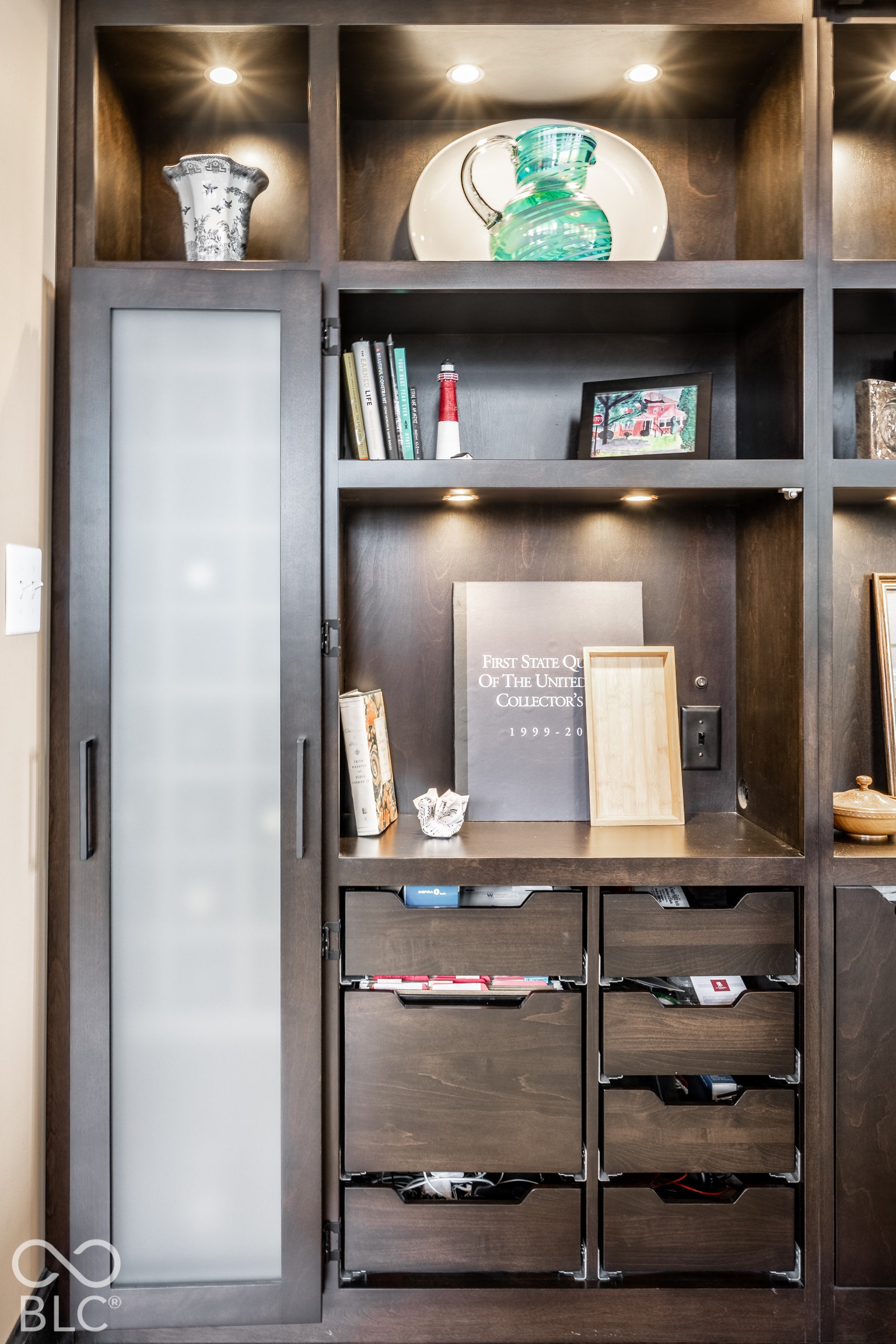 Built-in dark wood cabinetry featuring open shelving, integrated lighting, a frosted-glass panel door, and multiple pull-out drawers