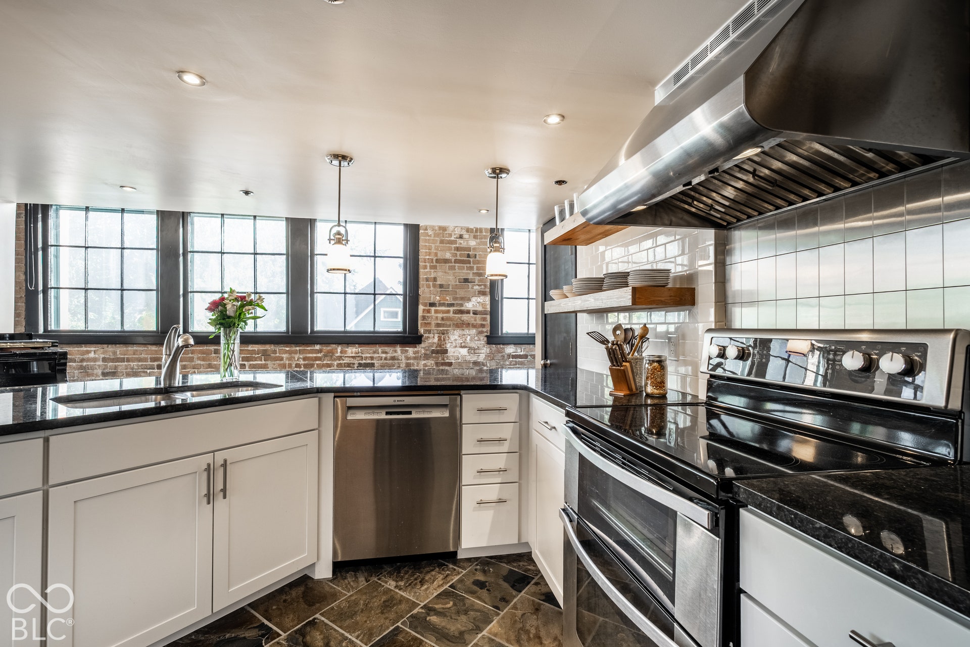 Stainless steel appliances, black countertops, white cabinetry, exposed brick, and recessed lighting