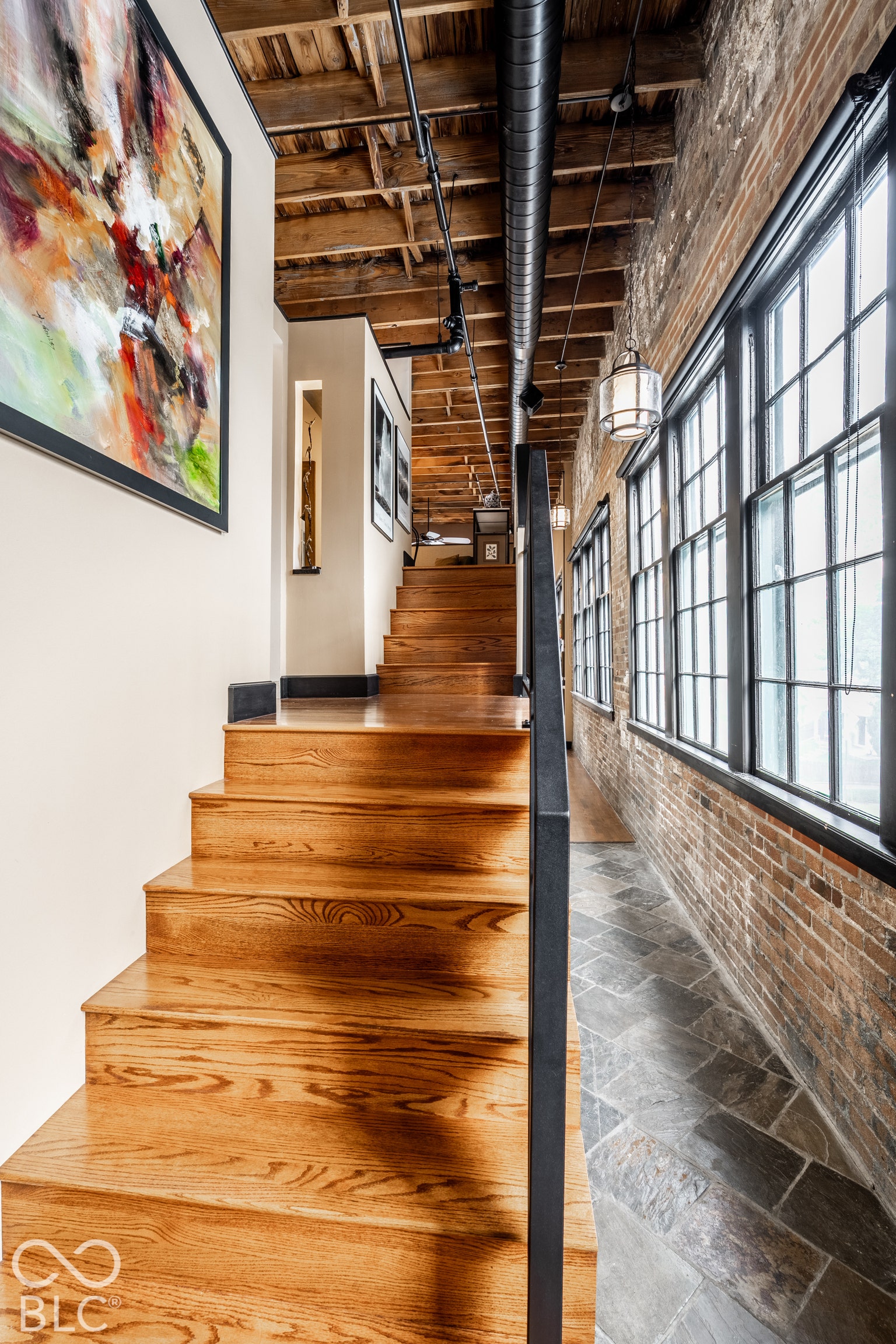 Hardwood staircase with metal railing, exposed brick wall, exposed wood ceiling, ductwork, and large pane windows