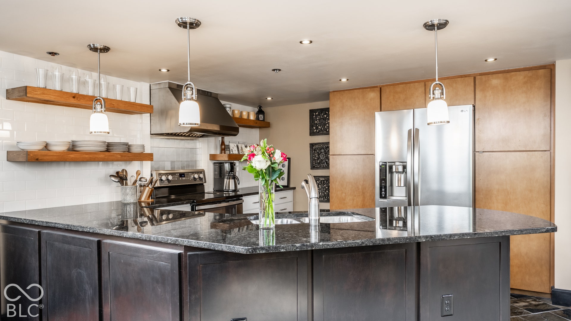 Kitchen featuring a large island with dark stone countertops, stainless steel appliances, open wood shelving, and recessed lighting