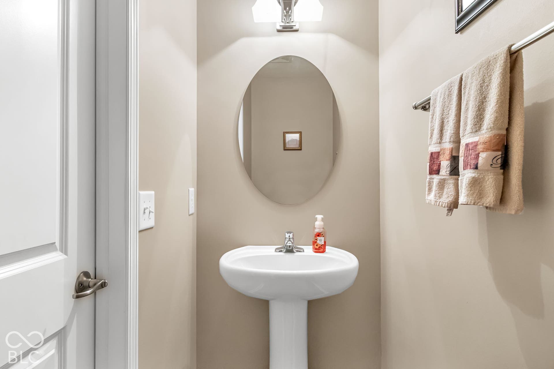Pedestal sink with chrome faucet, oval mirror, and wall-mounted light fixture