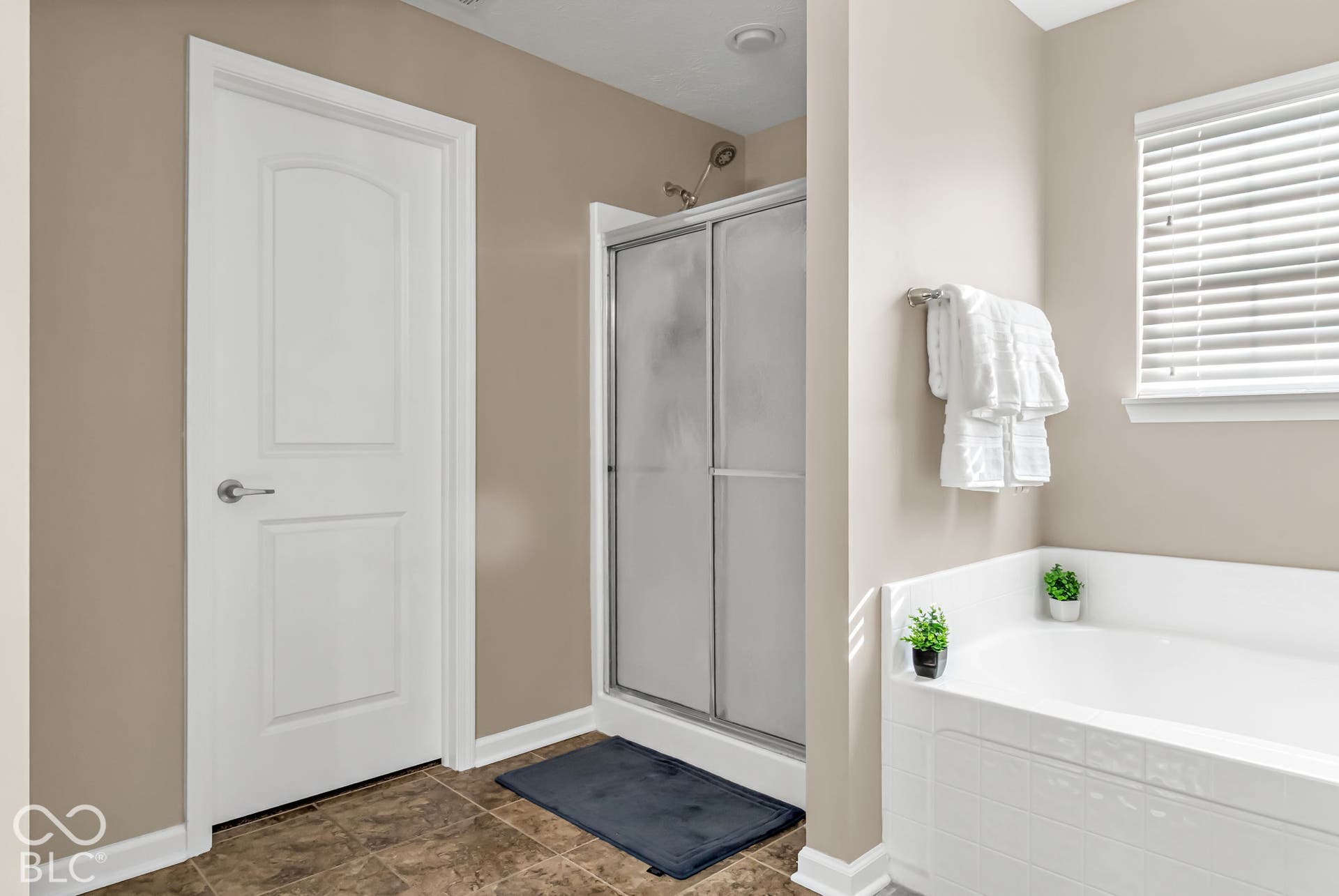 Deep soaking tub with a tiled surround, adjacent shower with sliding glass doors, and a window with blinds