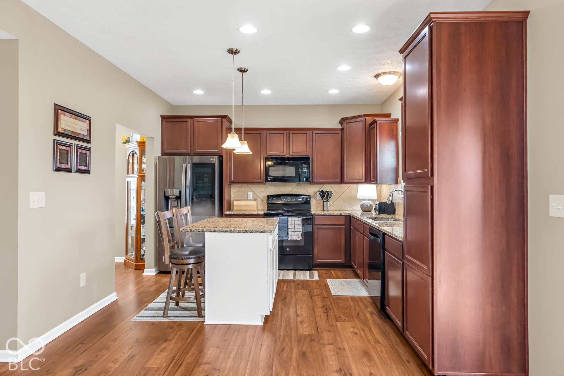 Kitchen featuring wood-finish flooring, dark wood cabinetry, stainless steel appliances, and a central island with a granite-style countertop