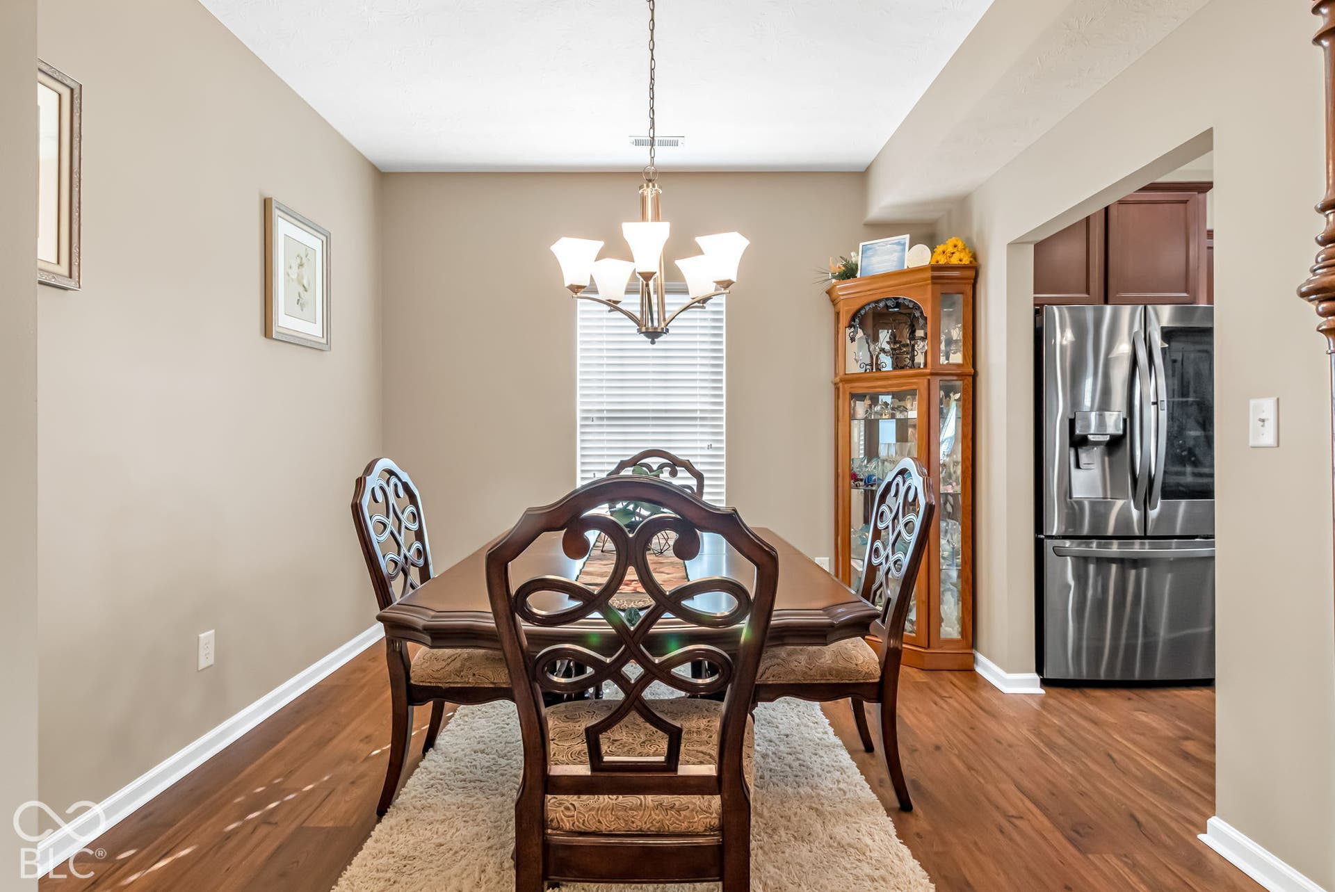 Dining area with wood-finish flooring, a contemporary chandelier, and a window with blinds