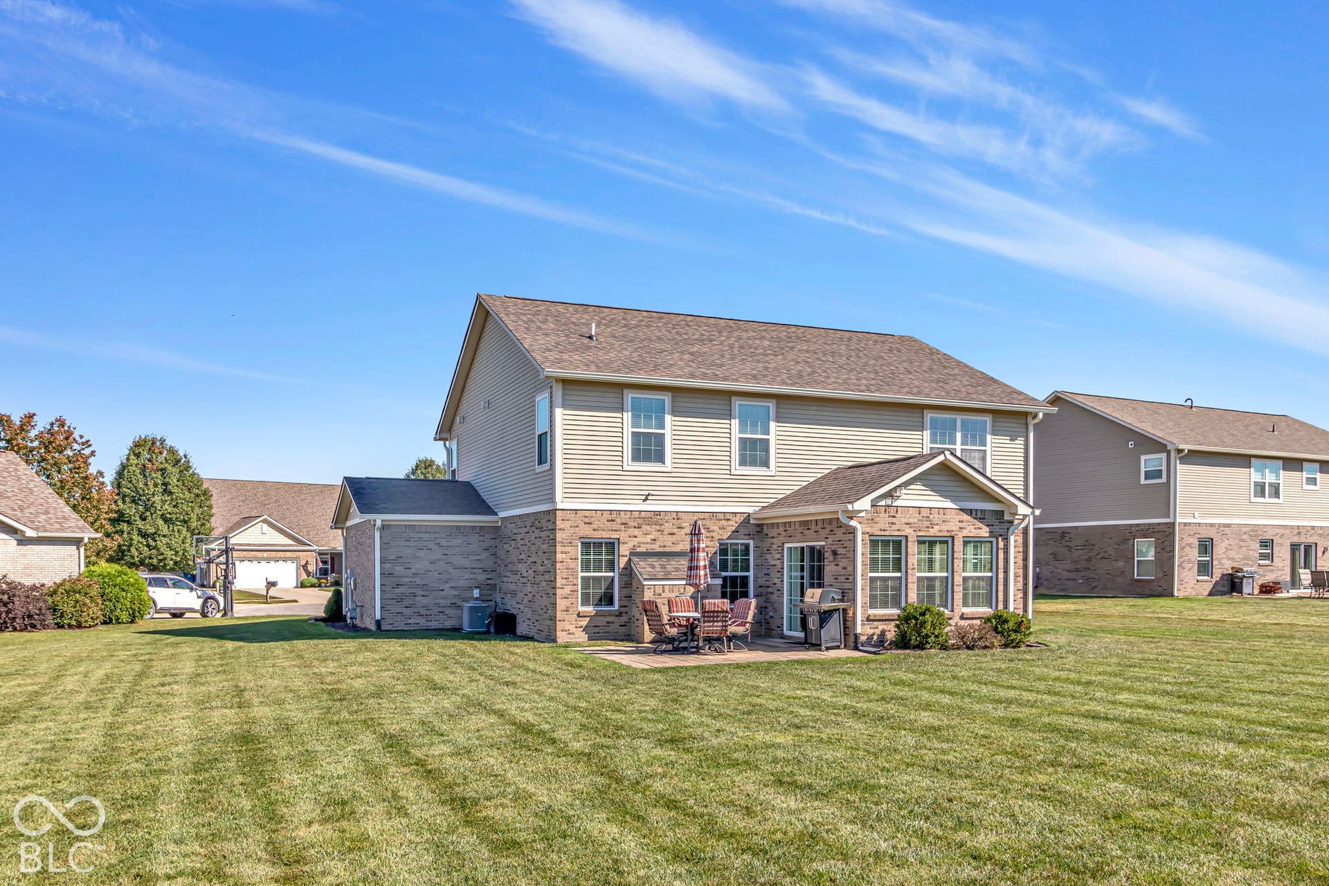 Expansive backyard featuring a manicured lawn, brick and siding exterior, a patio area, multiple windows, and a built-in sunroom