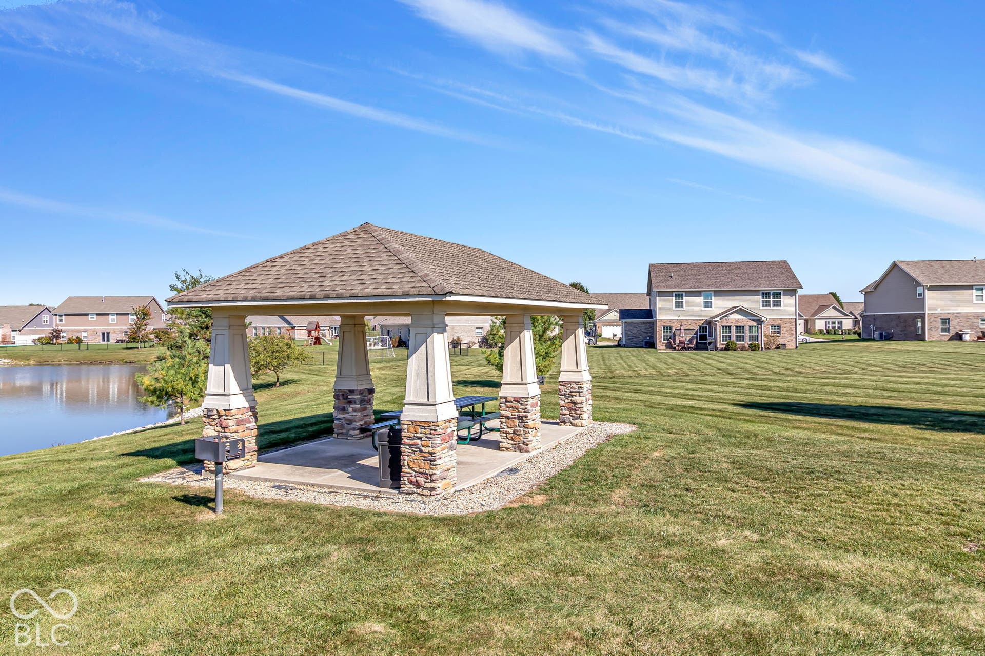 Gazebo with stone-clad columns and shingle roof, concrete pad, picnic table, and grill
