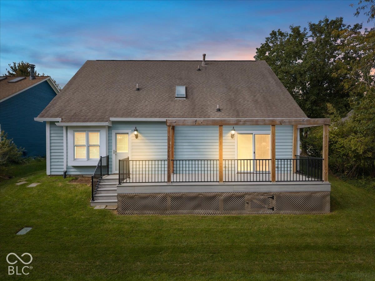 Rear exterior featuring light blue horizontal siding, an elevated deck with metal balusters, a wooden pergola, lattice skirting, and a shingled roof with a skylight
