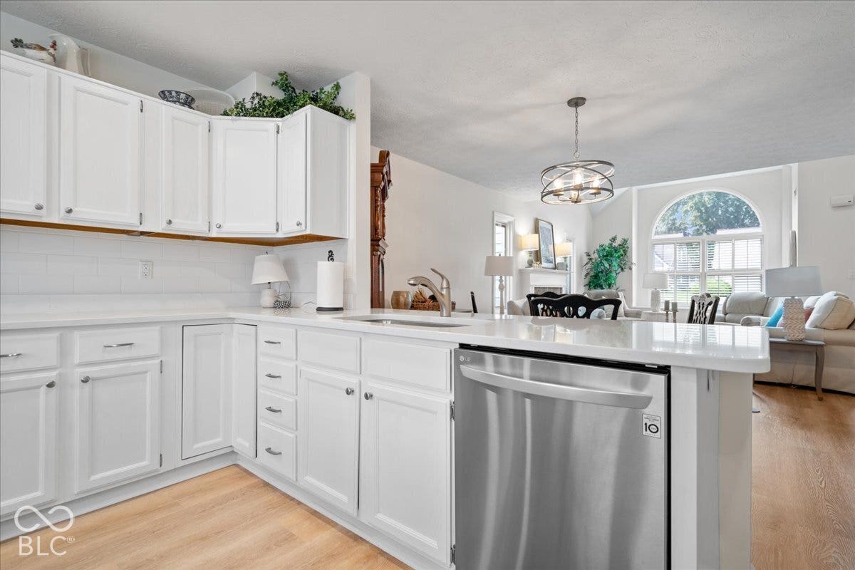 Kitchen featuring white cabinetry, solid-surface countertops, stainless steel dishwasher, and wood-finish flooring