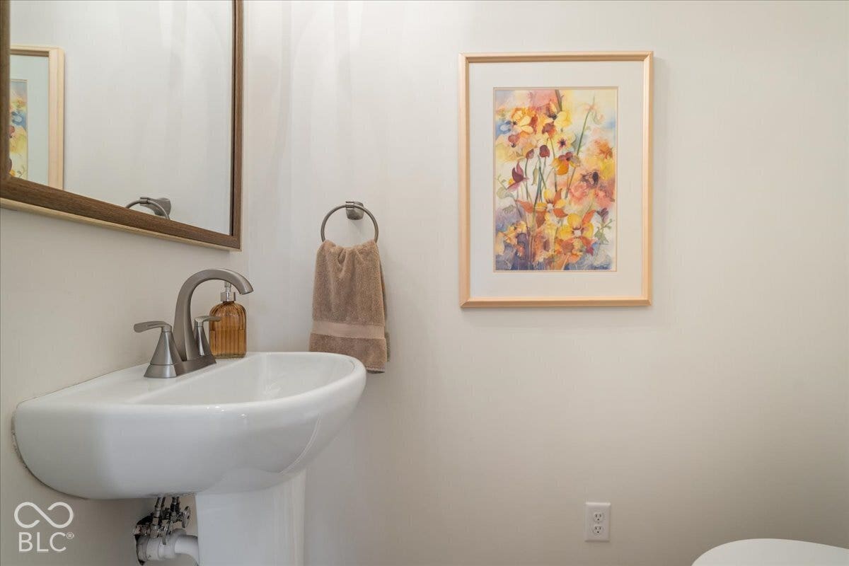 White porcelain pedestal sink with a brushed nickel widespread faucet, framed wall-mounted mirror, and brushed nickel circular towel ring