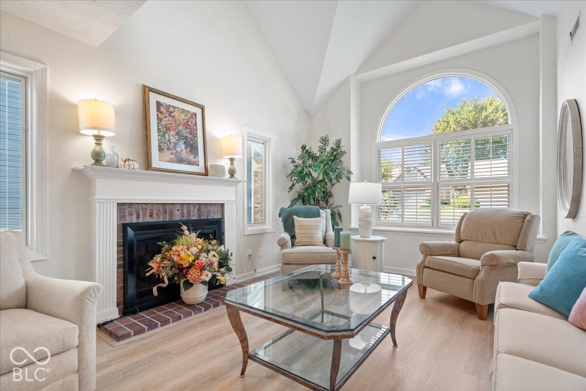 Vaulted ceilings, arched window, brick-surround fireplace with a classic mantel, and wood-finish flooring
