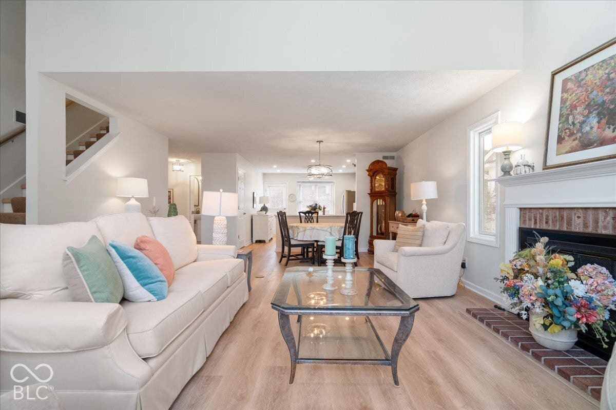 Open living area featuring vaulted ceilings, wood-finish flooring, a brick-surround fireplace with a mantel, and recessed lighting
