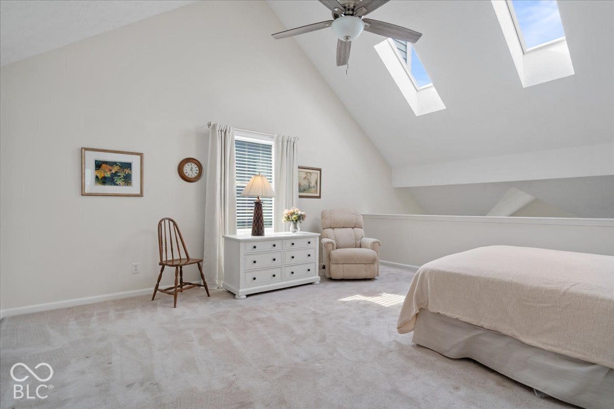 Vaulted ceilings featuring dual skylights, a ceiling fan with integrated lighting, and neutral carpeting. Currently used as upstairs bedroom