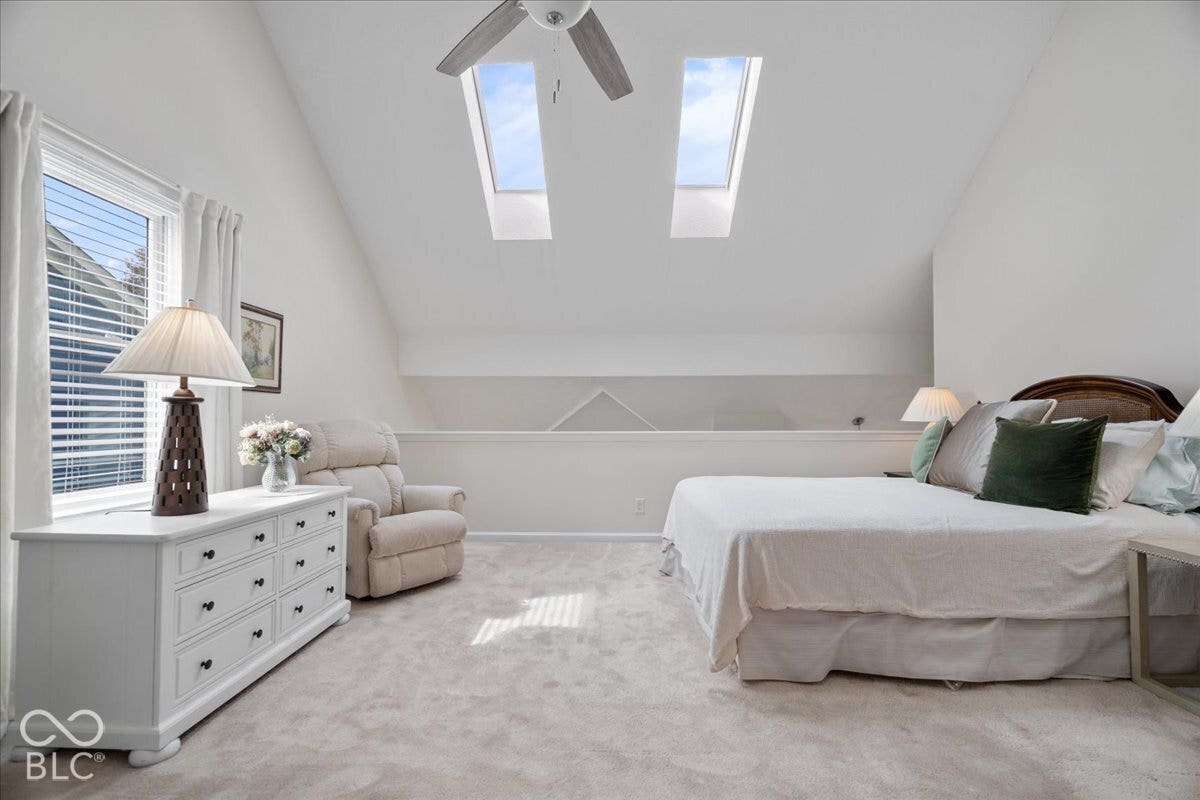 Vaulted ceiling featuring dual skylights, a ceiling fan, and carpeted flooring. Currently used as bedroom.  Access to attic storage