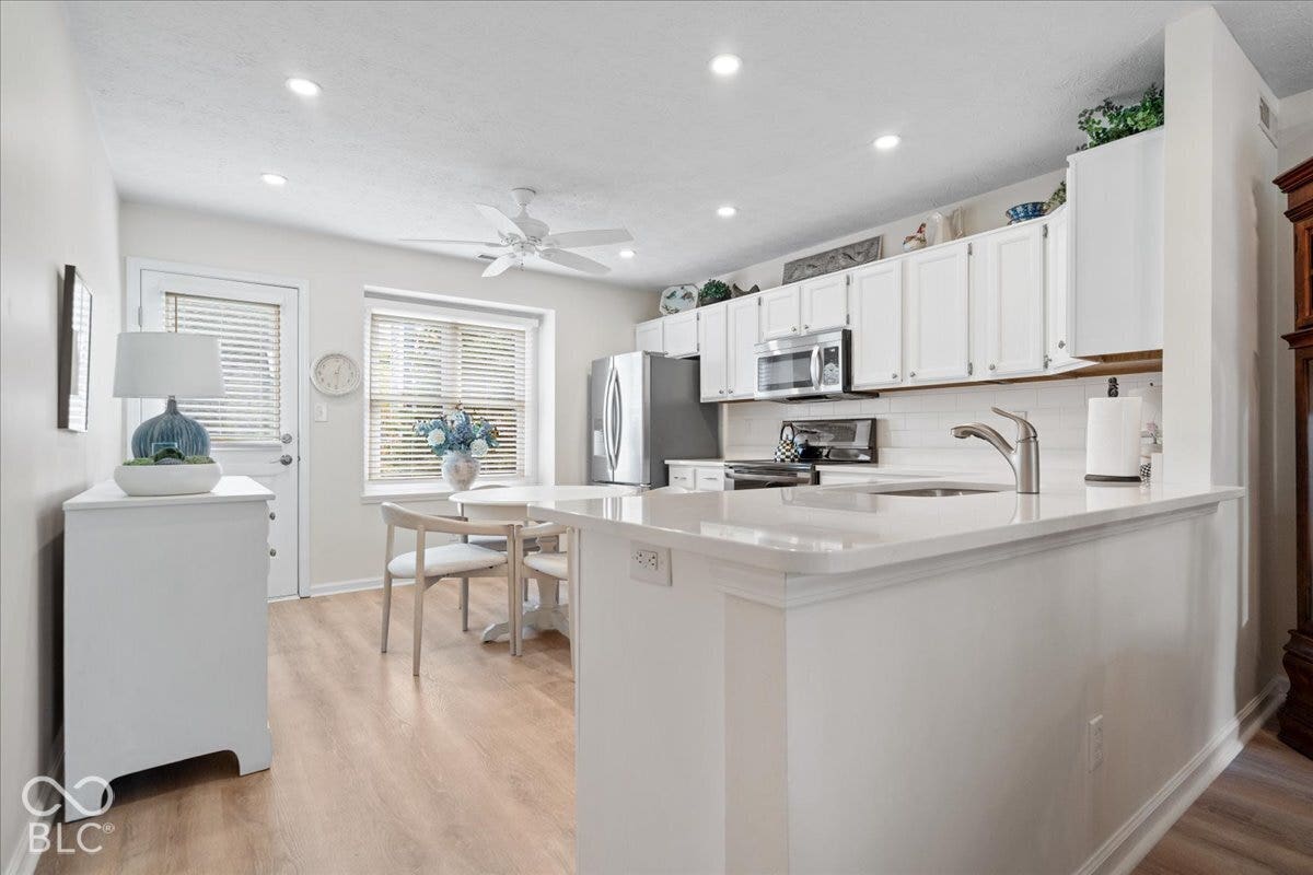 Kitchen featuring white shaker-style cabinetry, solid-surface countertops, recessed lighting, and wood-finish flooring